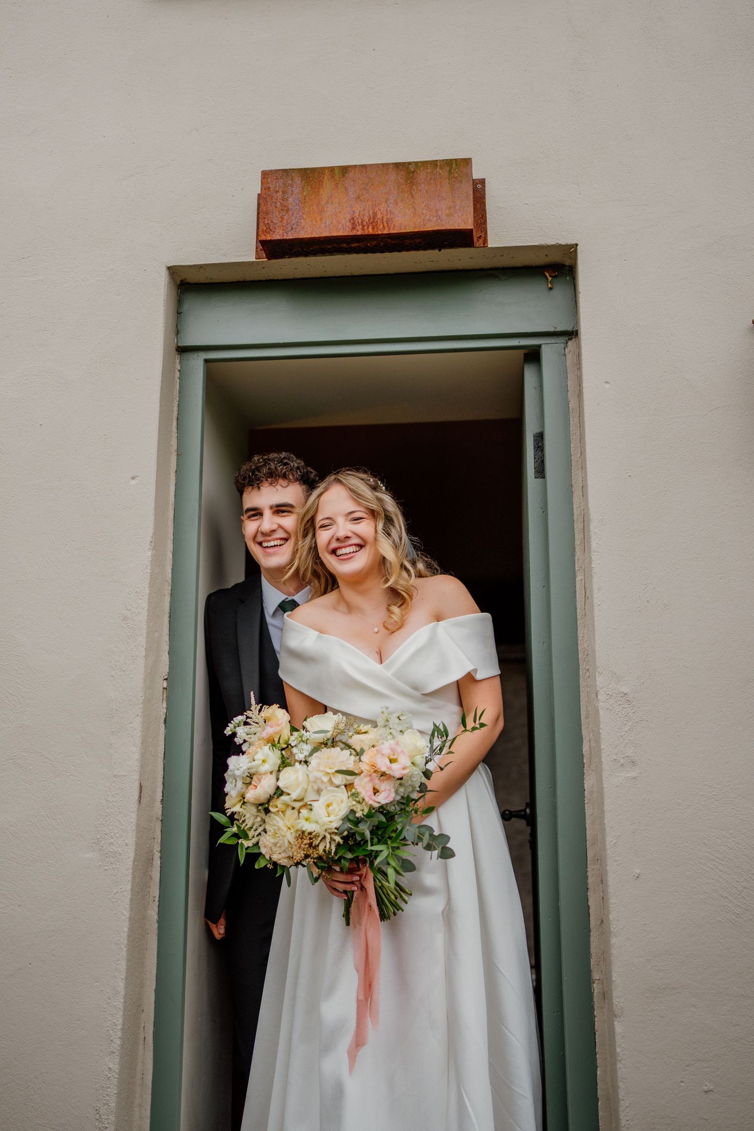 A couple stands in a doorway sharing a joyful moment during their wedding day.