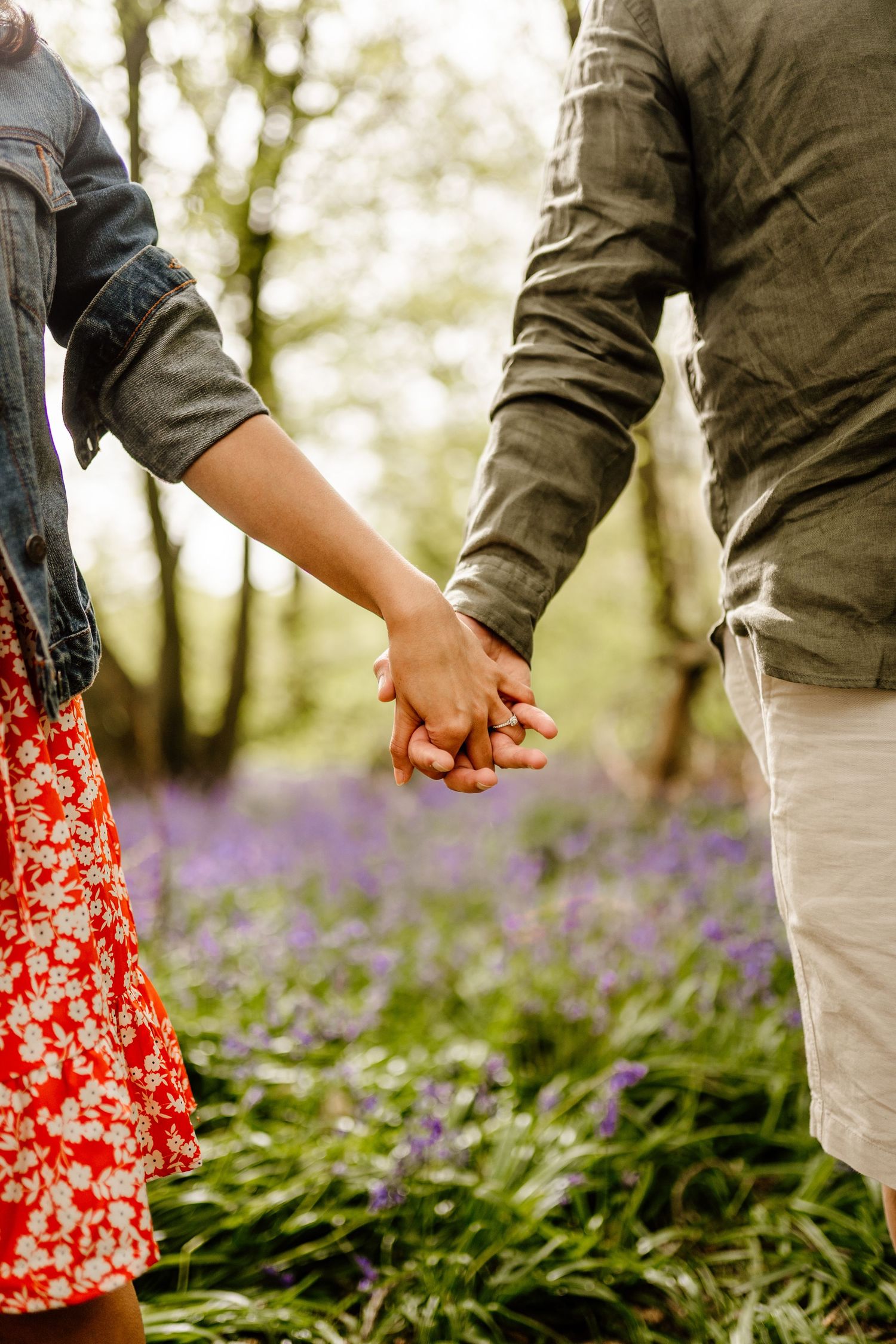 A couple holds hands in a romantic forest setting with purple bluebells in Hertfordshire.