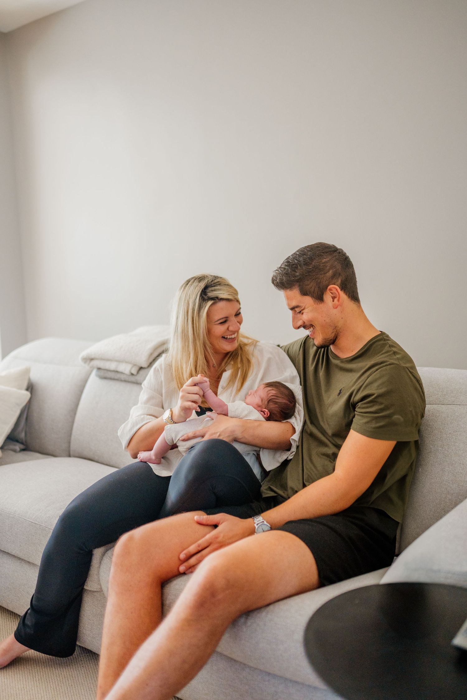 New parents sharing intimate moments with their baby on a grey couch.