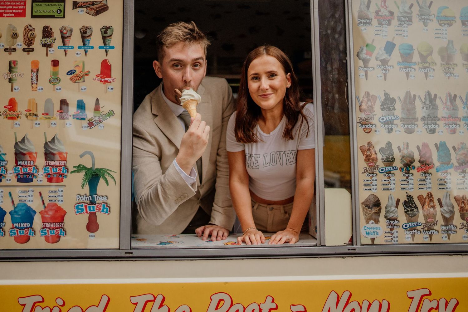 A playful couple poses in an ice cream truck window surrounded by colorful menu signs.