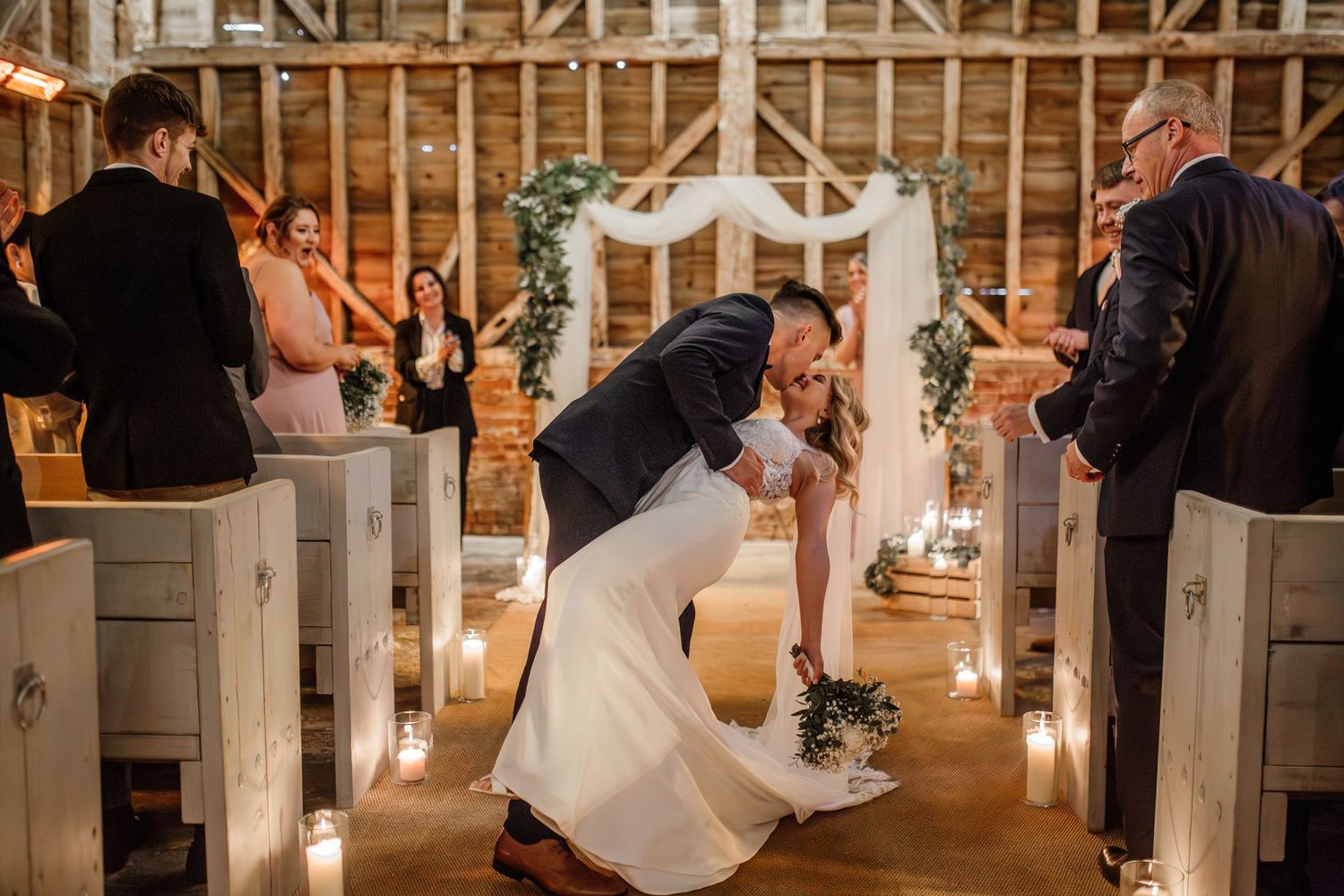 Wedding reception celebration inside a rustic wooden barn venue with string lights.