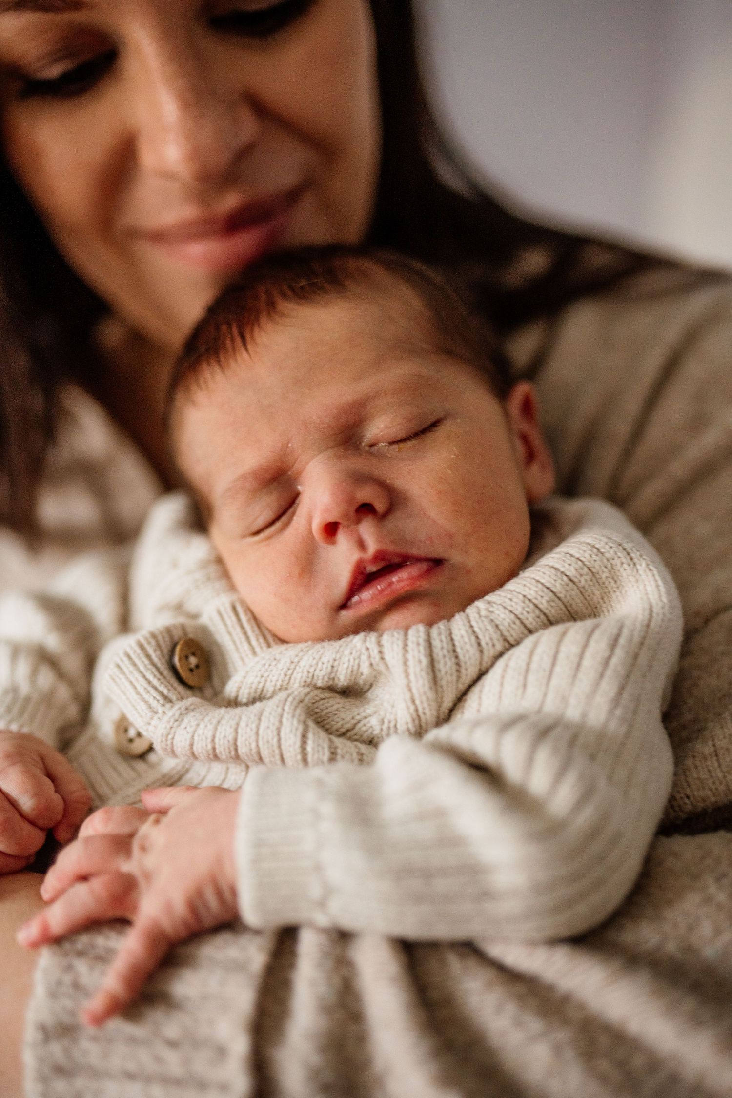 Sleeping newborn in cozy white sweater captured in intimate close-up shots.