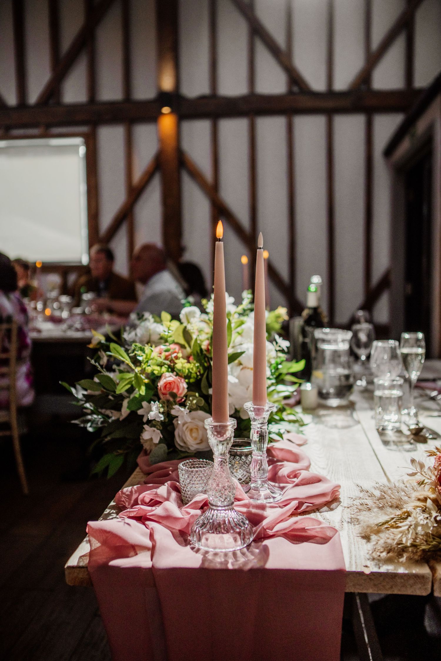 Elegant table setting with pink linens, candles and floral arrangements in rustic barn venue.