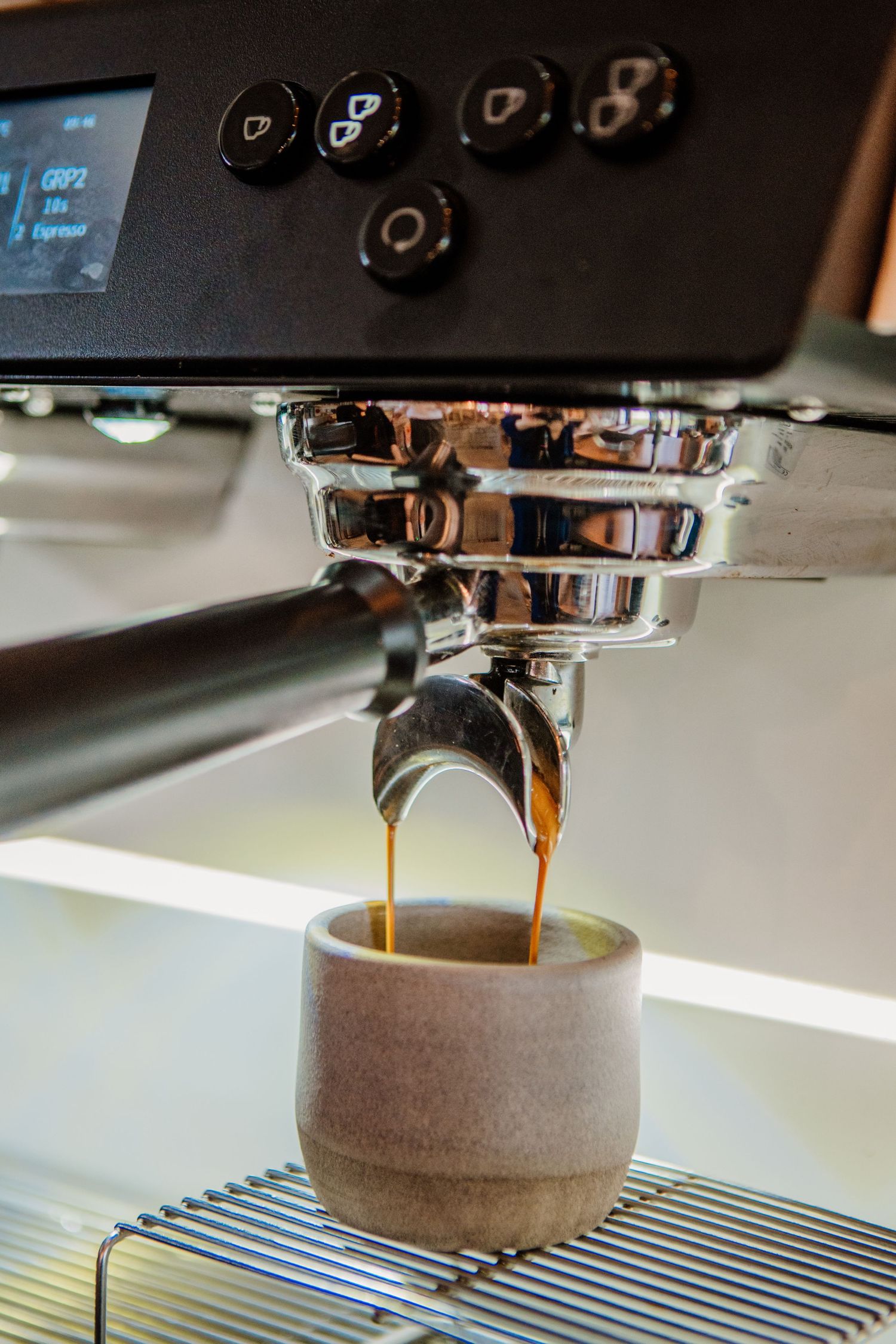 Close-up shot of espresso coffee being extracted from a portafilter into a gray ceramic cup on a striped surface.