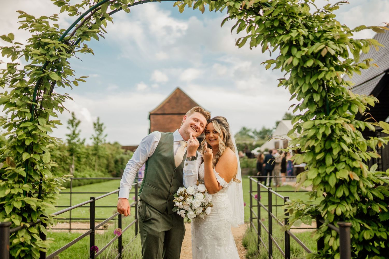 A couple shares a joyful moment under a natural green archway at their outdoor wedding celebration.