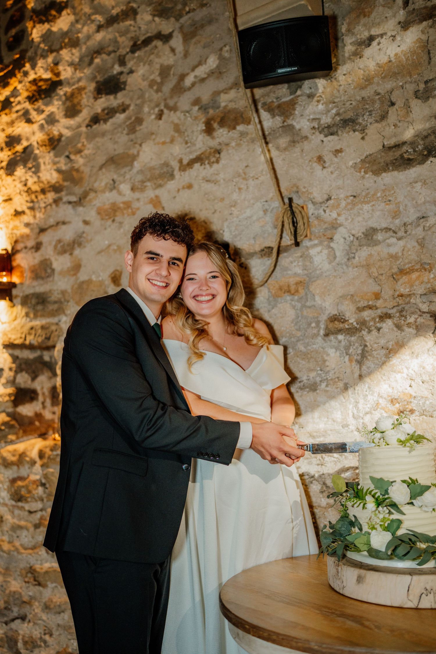 Couple embraces against stone wall during intimate wedding reception moment.