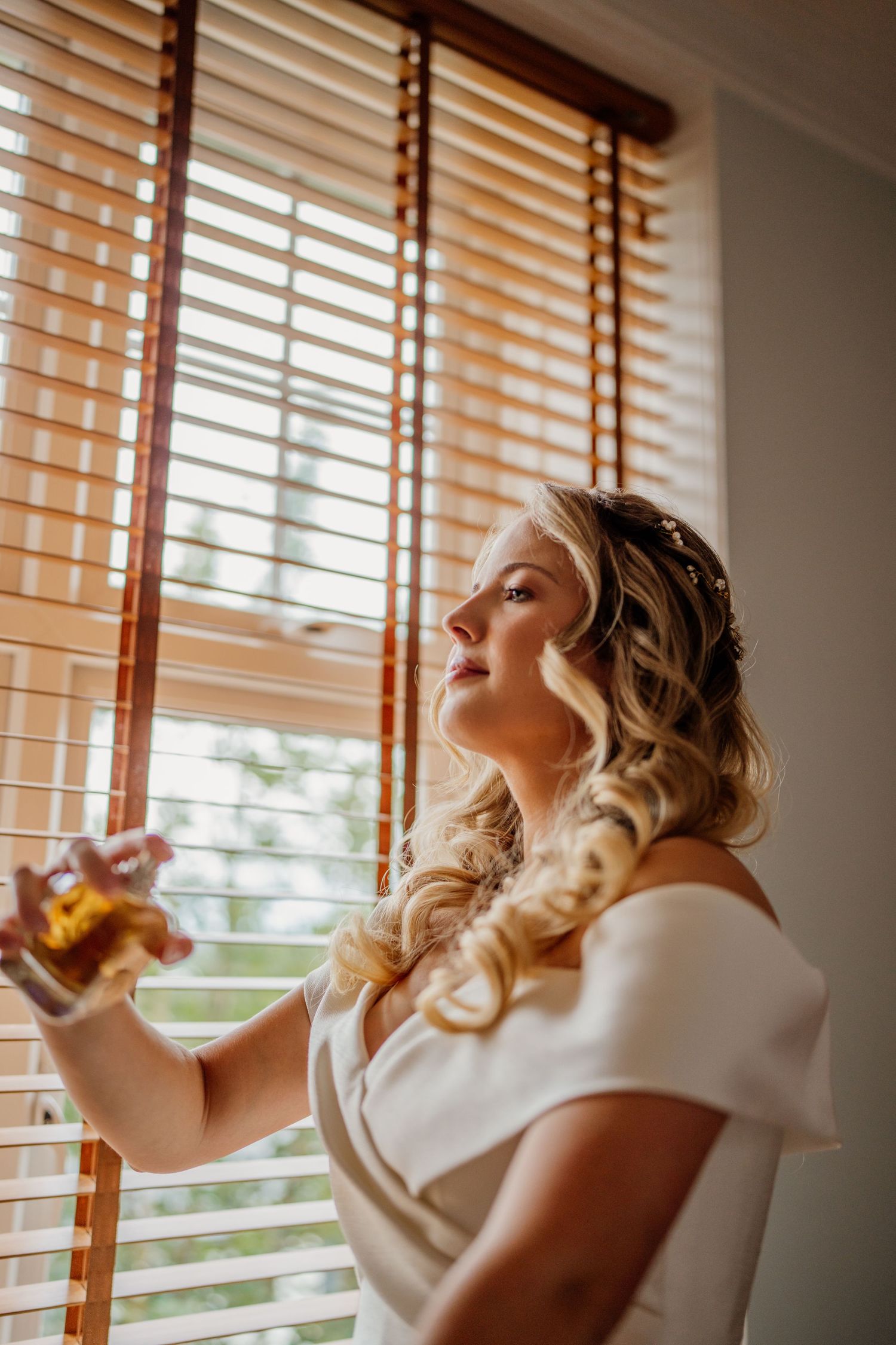 A person in white dress sits by window with wooden blinds.