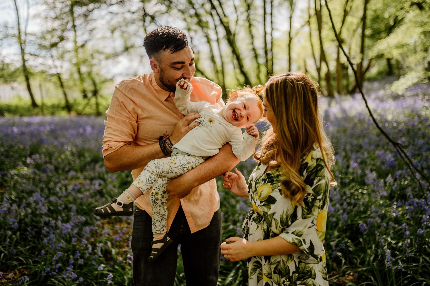 A family shares a joyful moment together in a spring forest filled with blooming bluebells in Hertfordshire.