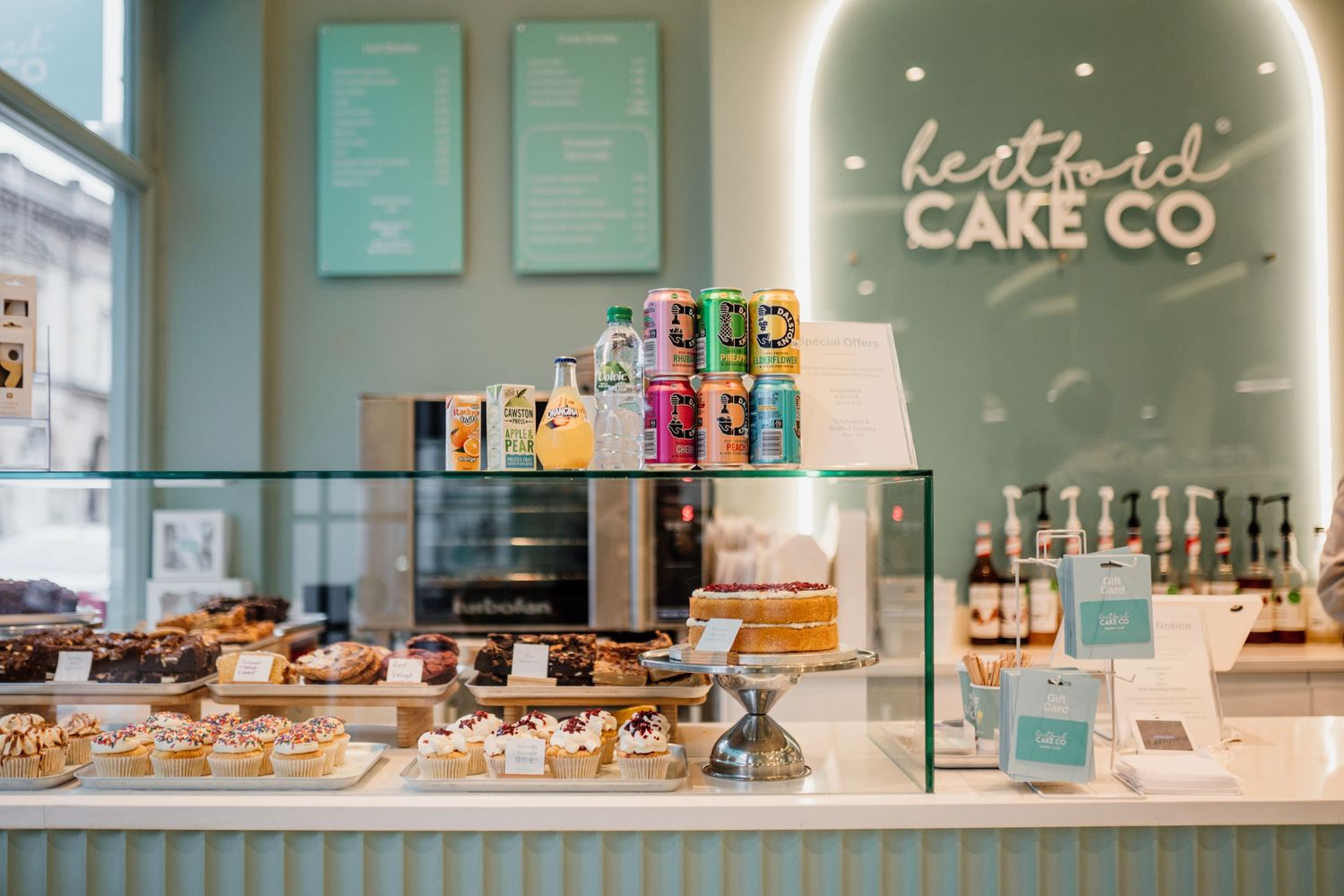 Modern cafe interior with turquoise walls and display cases showcasing baked goods and beverages.