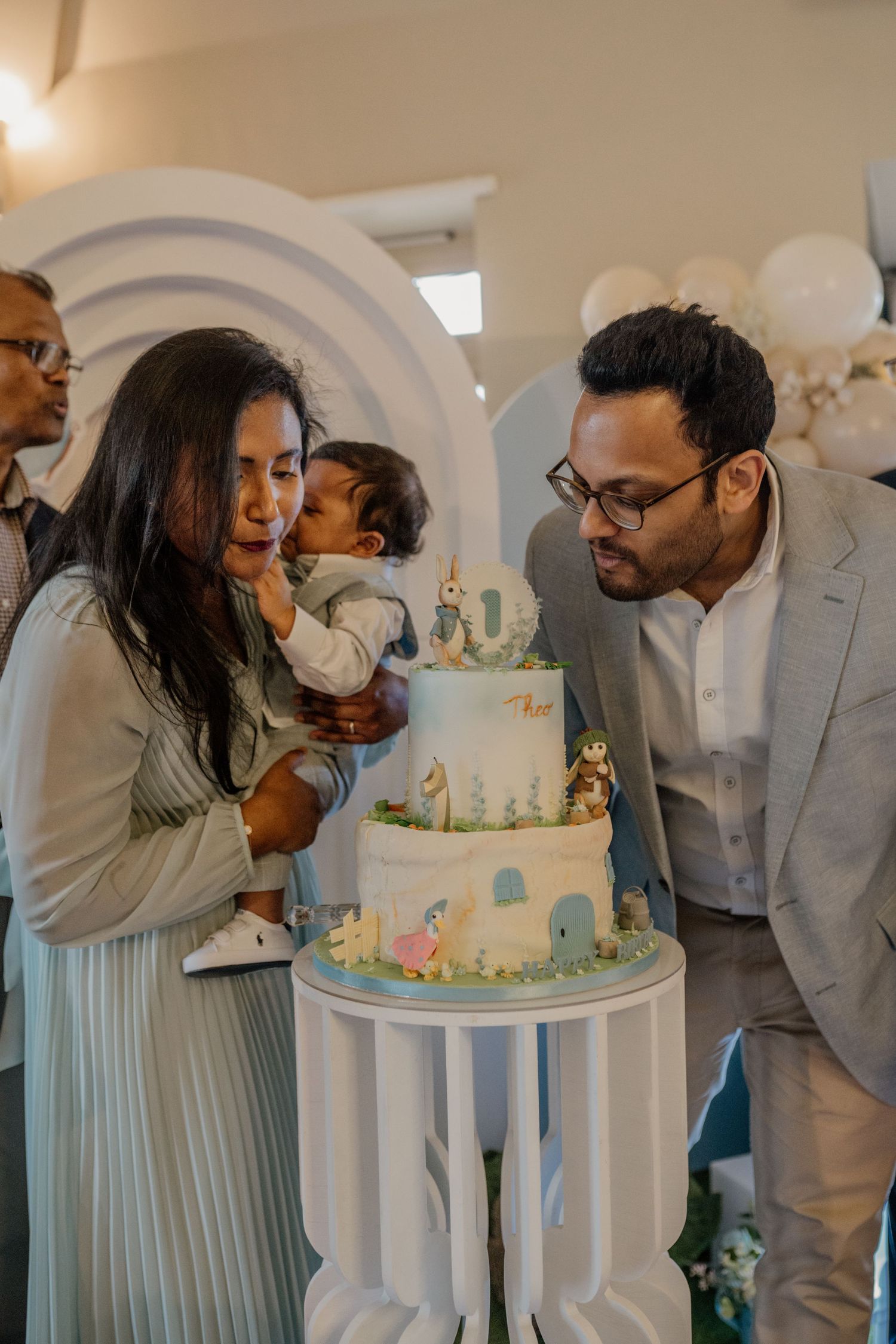Family gathering around a beautifully decorated white and blue celebration cake.