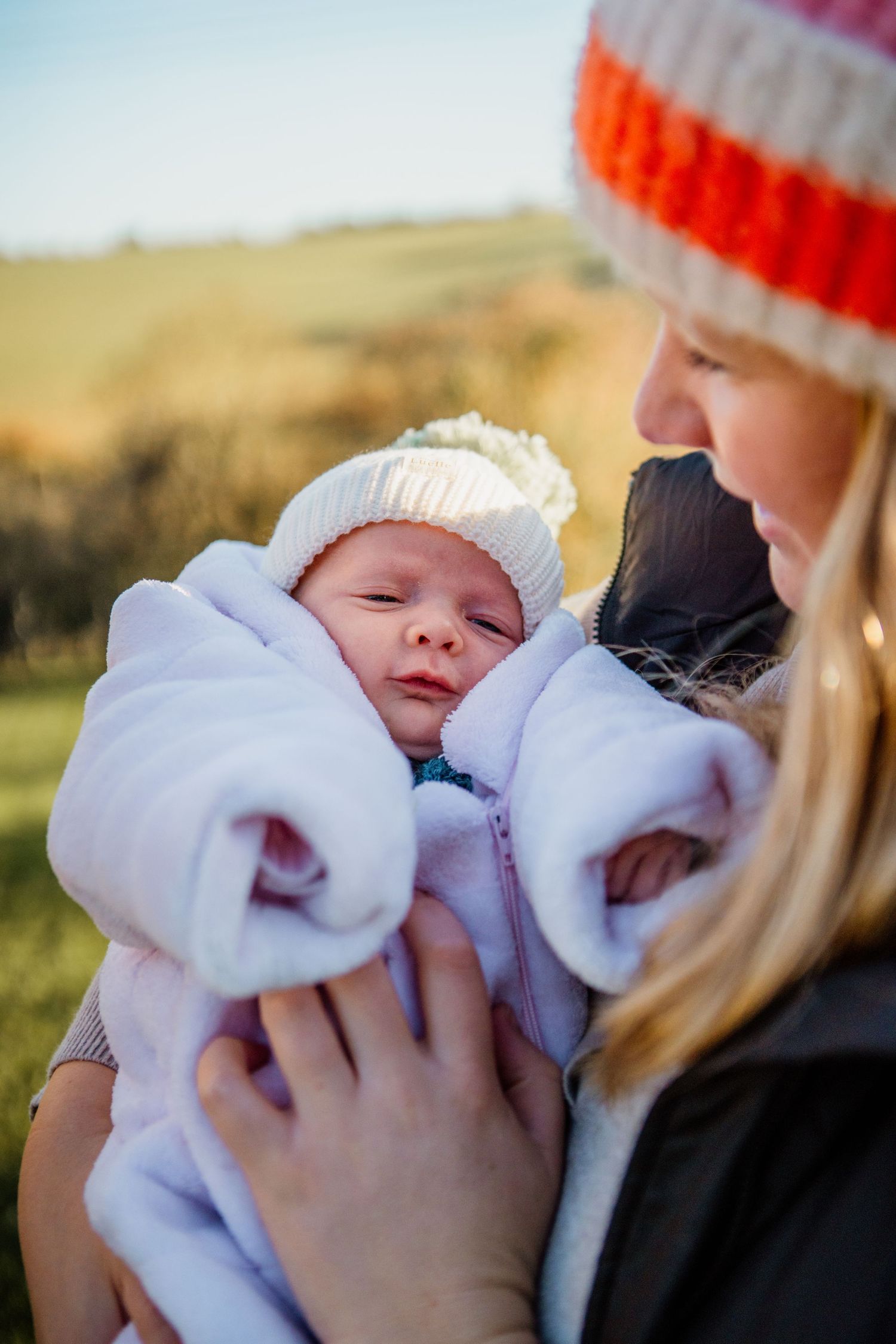 Sleeping newborn wrapped in white blanket outdoors against natural landscape.