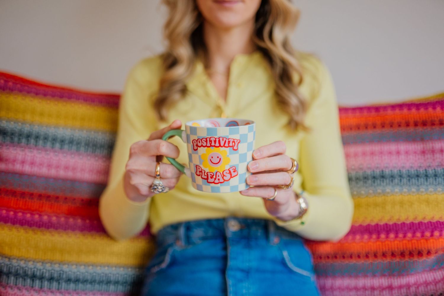 Person in yellow shirt holding a small product against colorful striped background.