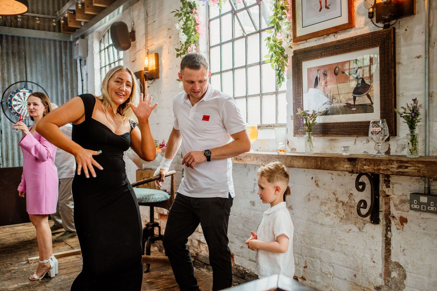People dancing and celebrating in an industrial-style venue with brick walls and large windows.