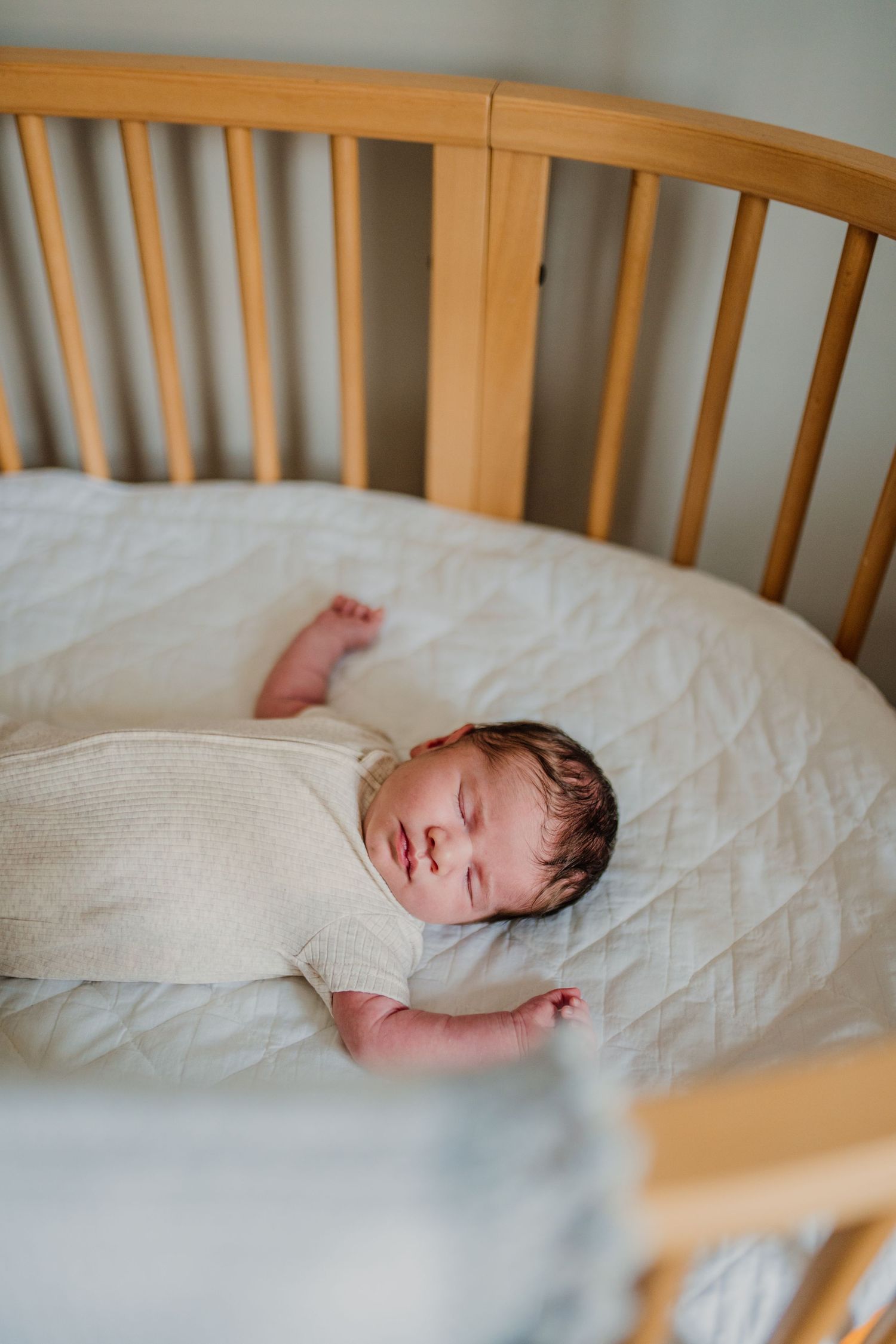 Sleeping newborn baby in wooden crib with white bedding.