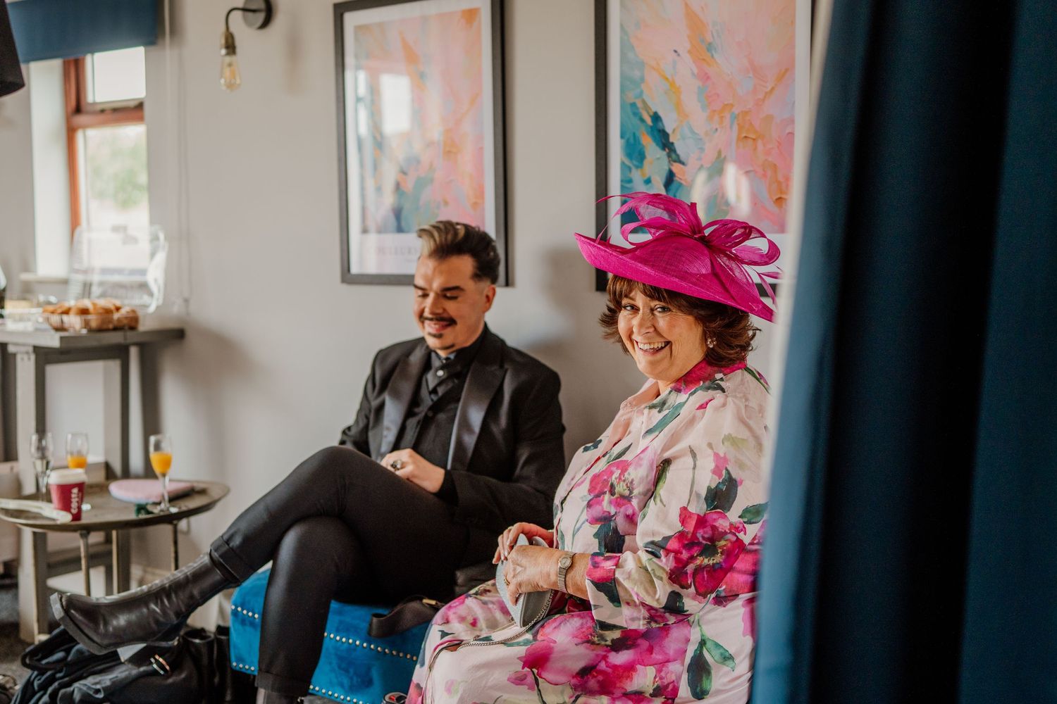 Guests in formal attire and colorful hats gather at a social event in an elegant indoor setting.