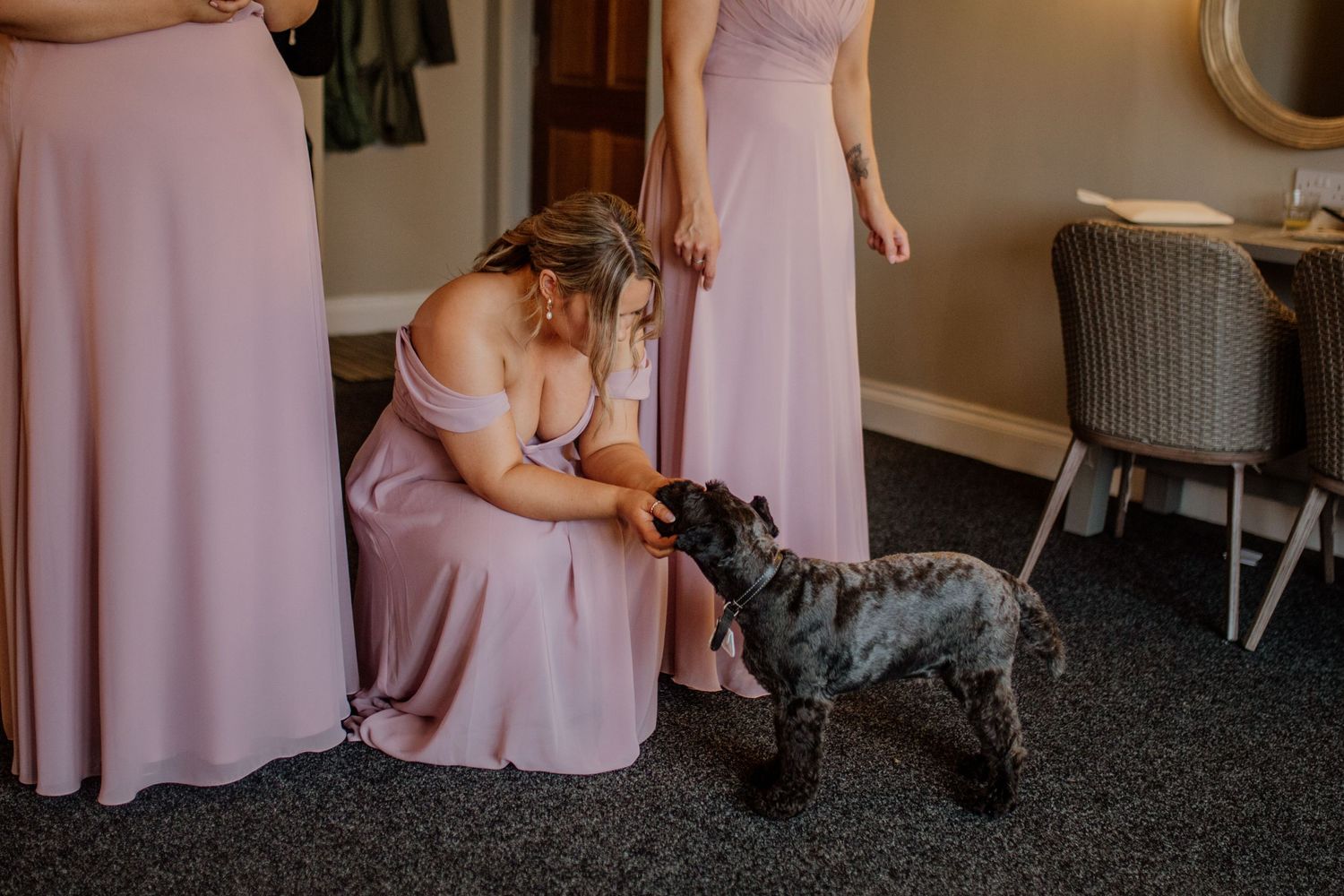 Bridesmaids in flowing pink gowns gathered in a warmly lit preparation room.