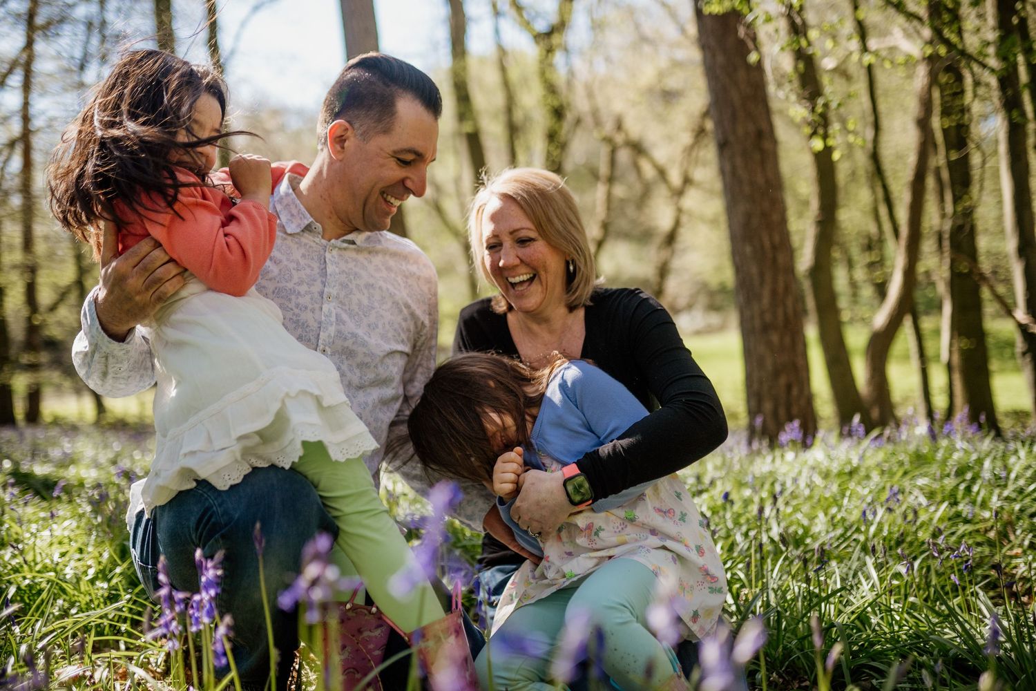 Family laughing together while sitting in a spring meadow with blooming purple bluebells in Hertfordshire
