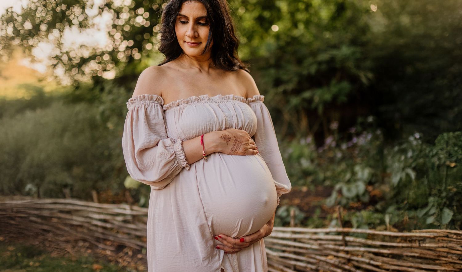 Maternity photo session in a white dress against natural outdoor backdrop.