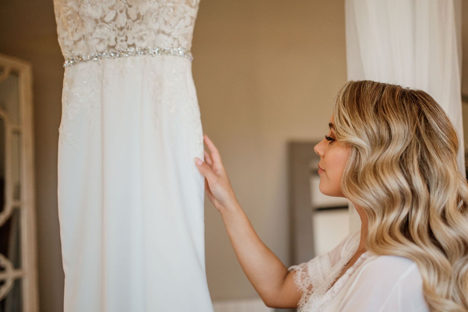 Close up details of an elegant lace wedding dress against a white wall.