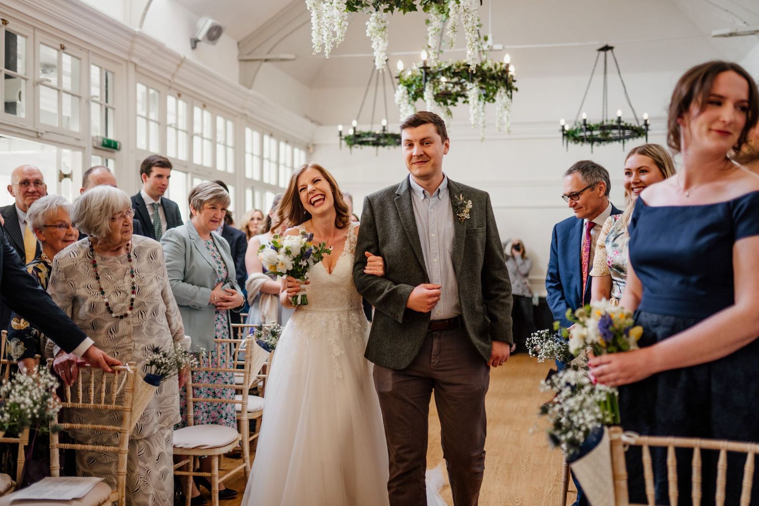 A wedding ceremony in a bright indoor venue with elegant chandeliers and floral decorations.