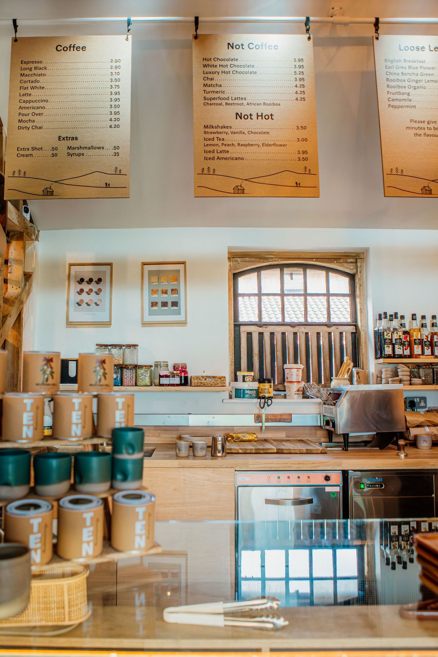 Modern coffee shop interior with wooden menu boards, counter displays, and minimalist decor in warm natural tones.