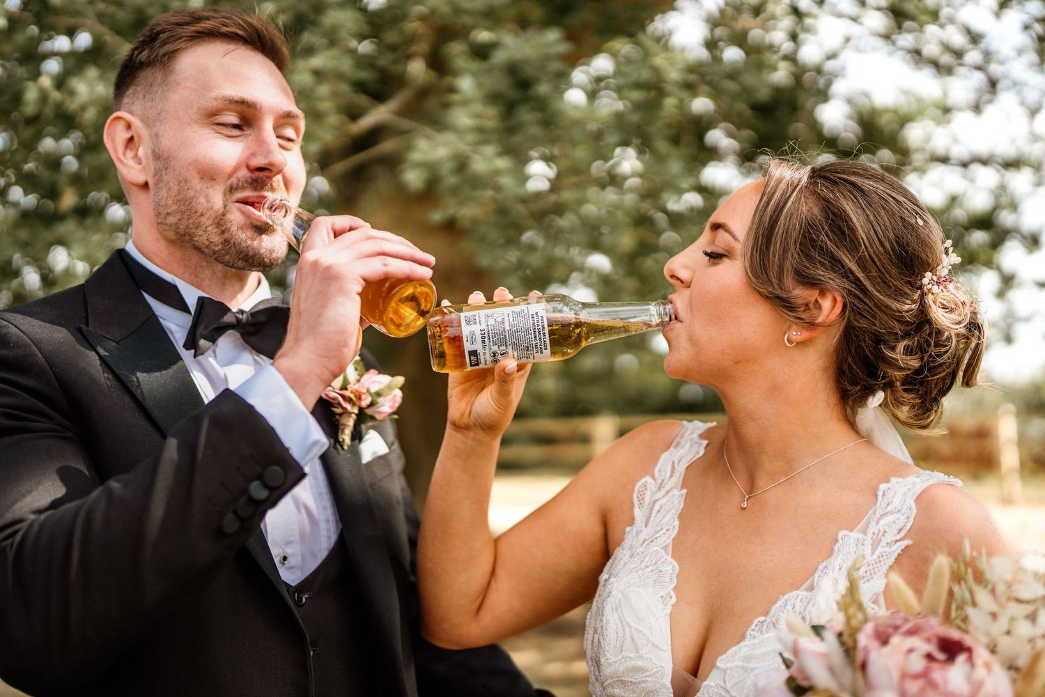 Wedding couple sharing drinks and laughter in an outdoor setting.