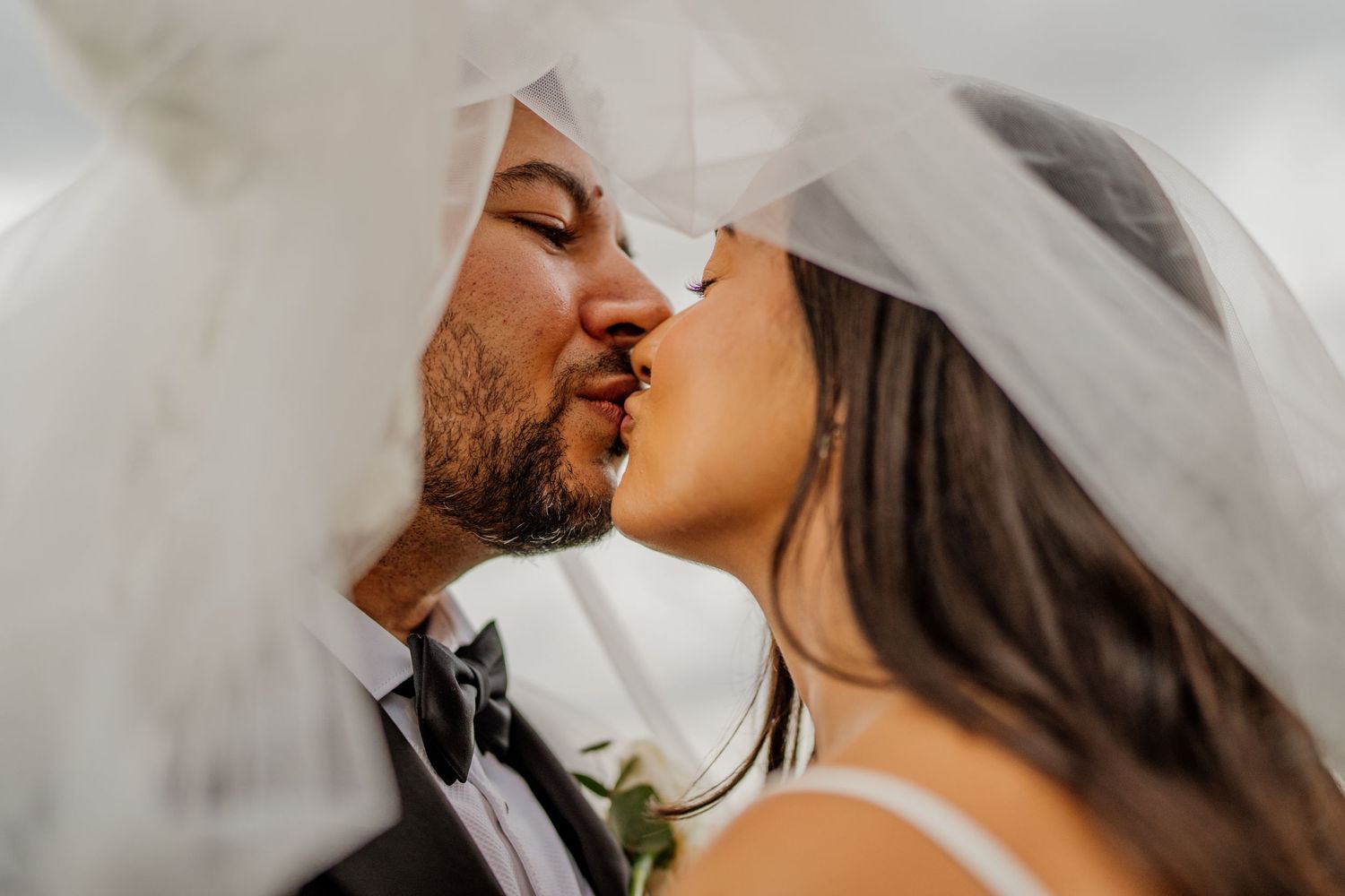 A romantic wedding photo showing a couple sharing a tender kiss while wearing traditional wedding attire.