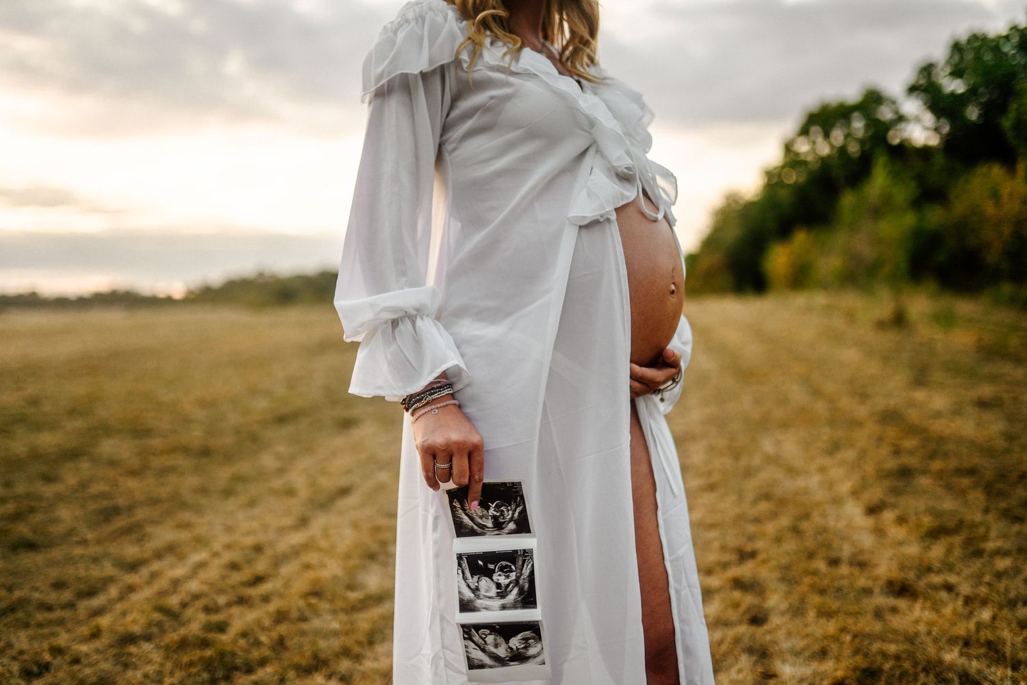 Maternity photo session in a golden field at sunset with ultrasound images.