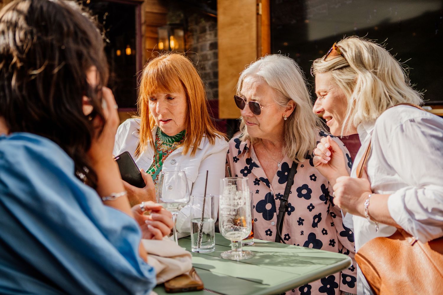 A group of people enjoying wine and conversation at an outdoor restaurant patio on a sunny day.