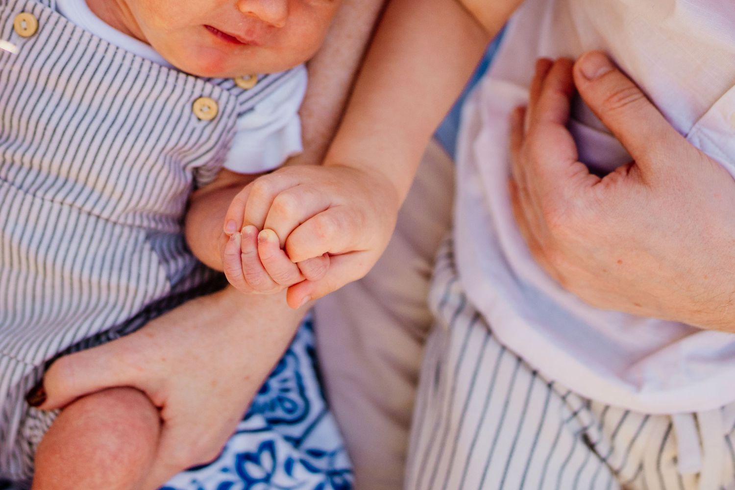 Close-up of tiny baby hands being gently held by adult hands in a tender moment.