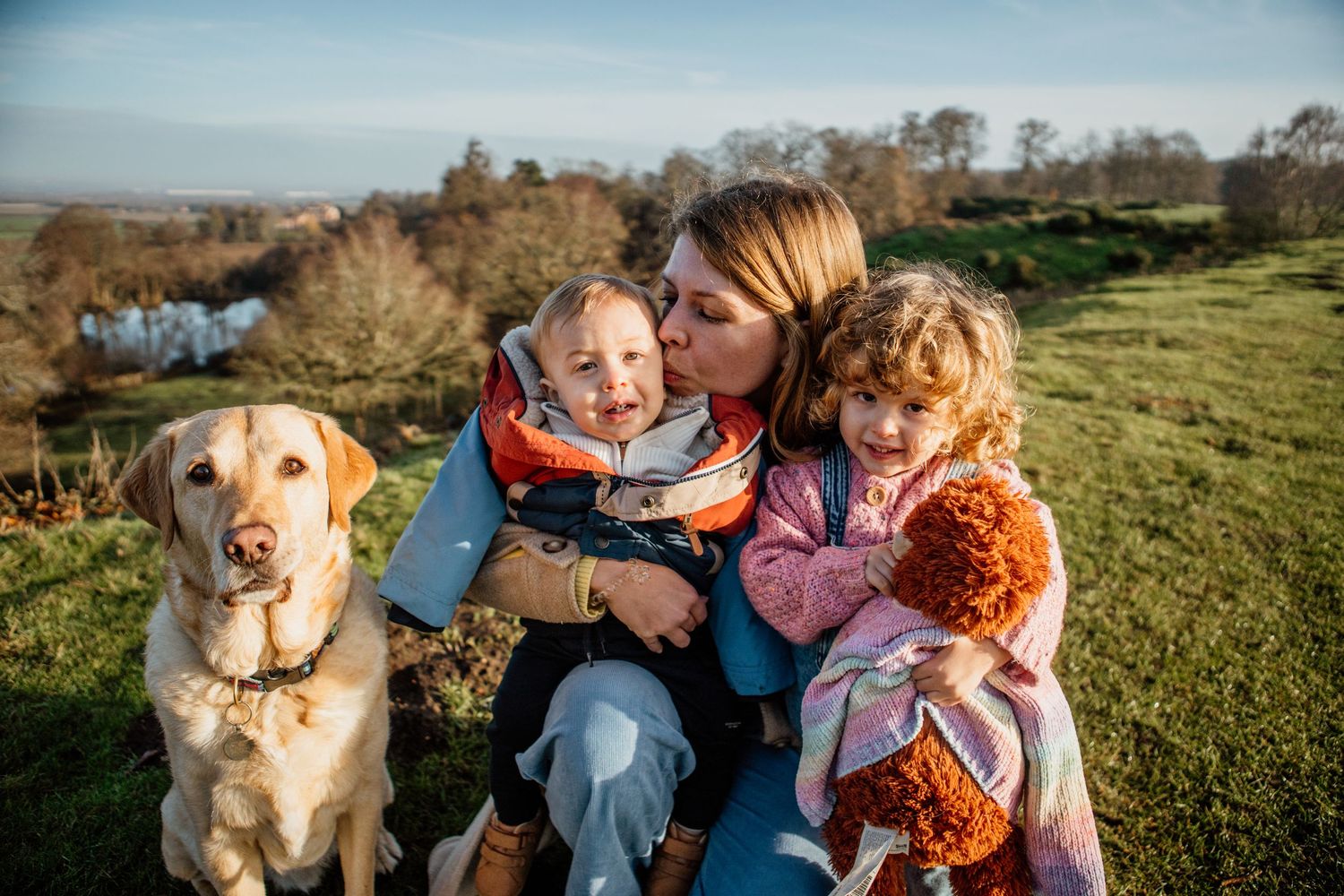 Family and golden retriever dog enjoying a sunny autumn day together on a grassy hillside.