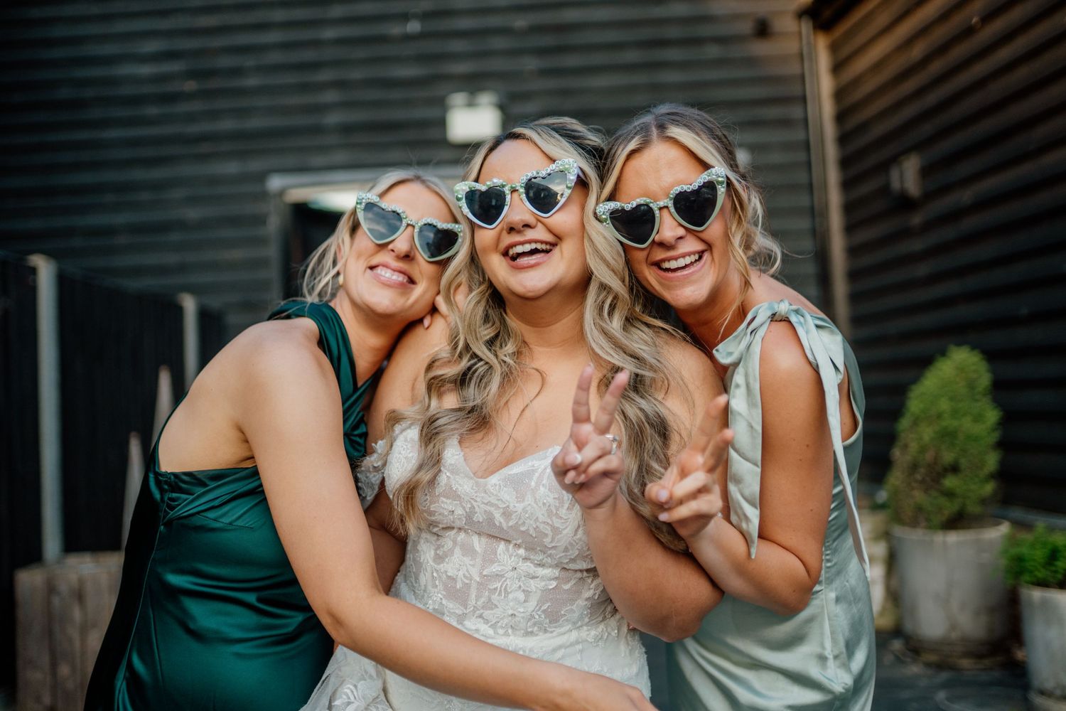 Wedding party wearing sunglasses and formal attire pose together while laughing outdoors.