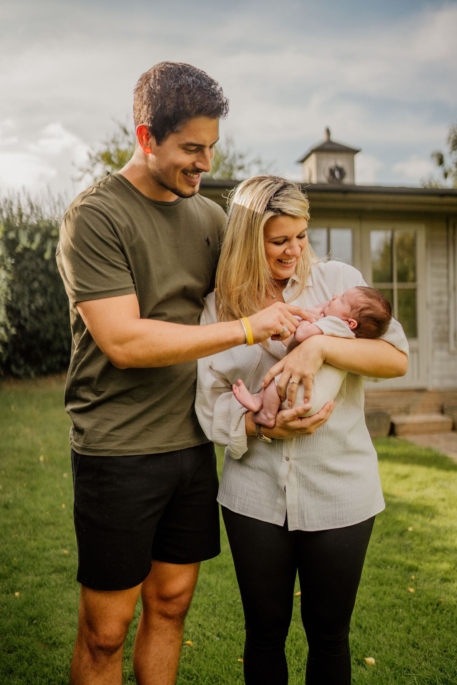 Family outdoor photoshoot with newborn baby on a grassy lawn near a building.