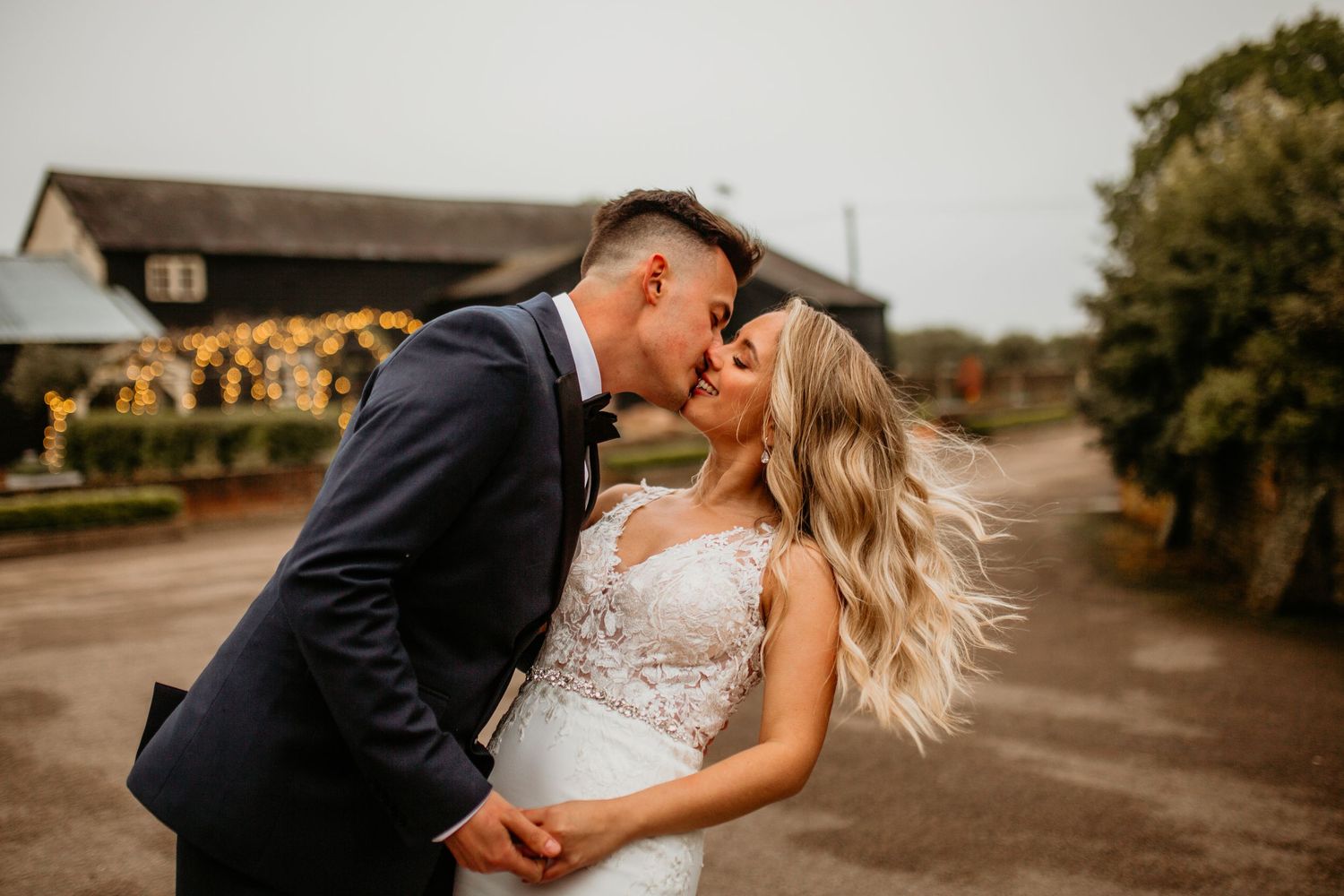 A couple in wedding attire share an intimate moment together during sunset on a rustic country road.
