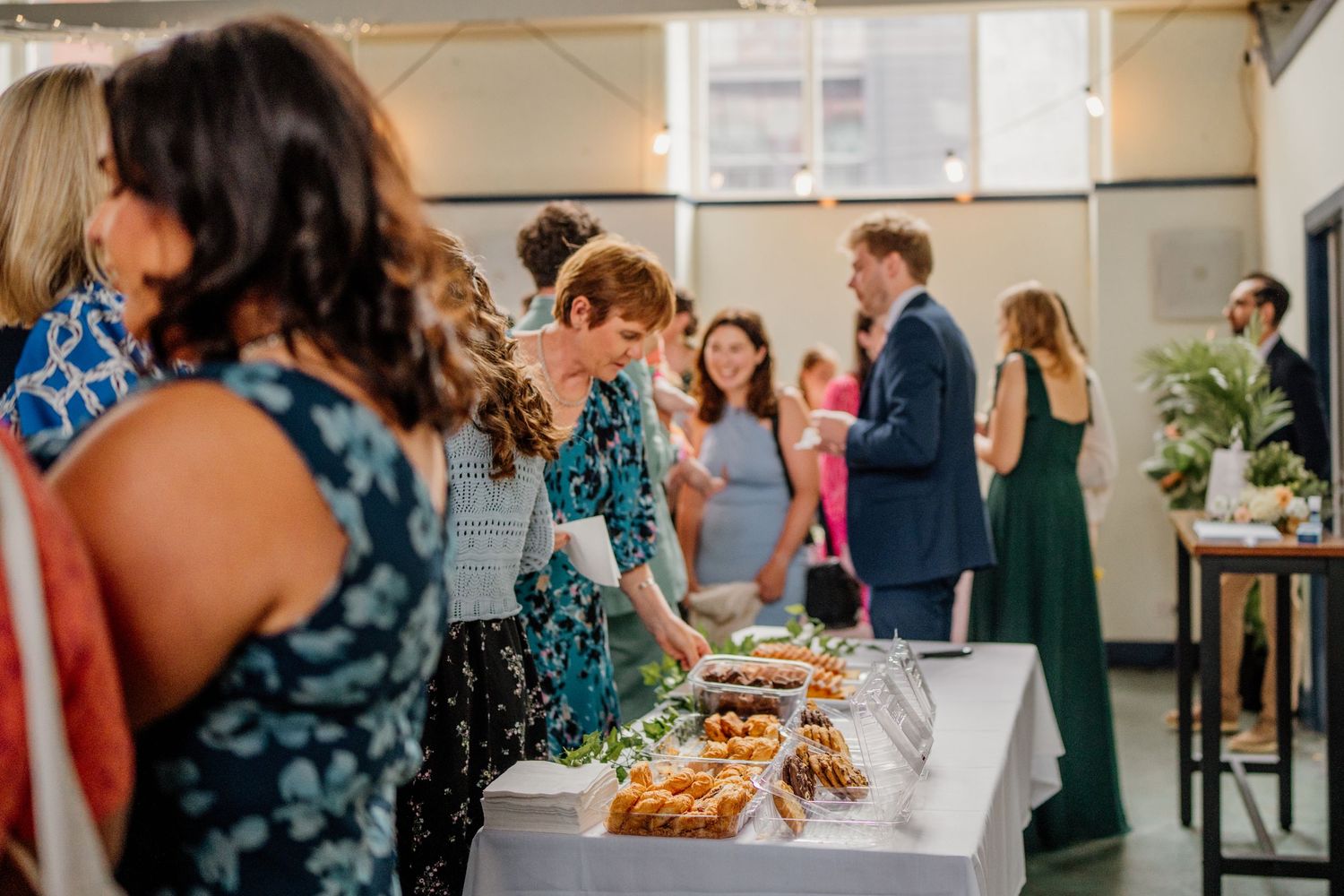 Guests gather around a buffet table with food and drinks at an indoor reception event.