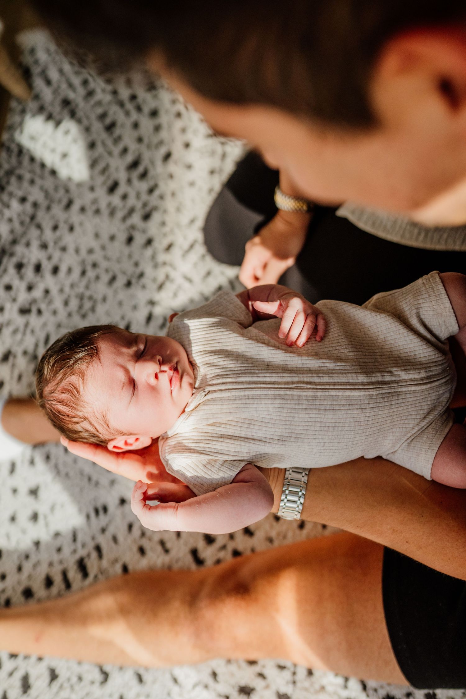 Close-up series of a baby in a gray onesie being held during a newborn photography session.