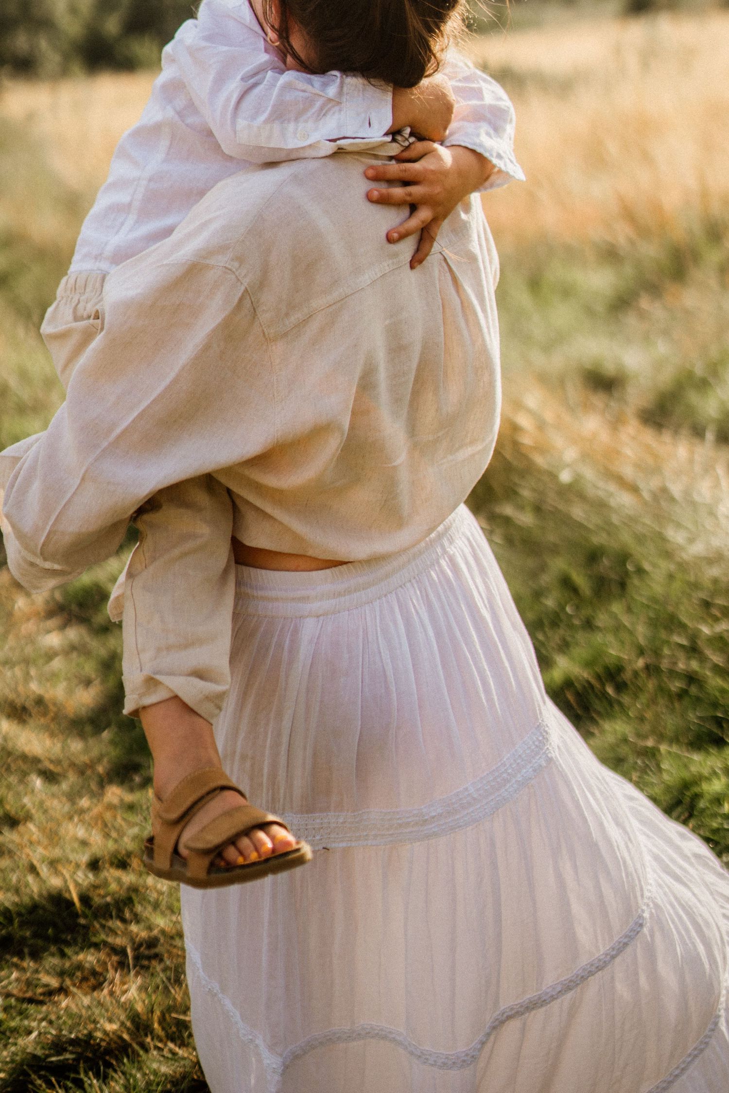Person wearing flowing white dress and top in a sunny meadow setting.