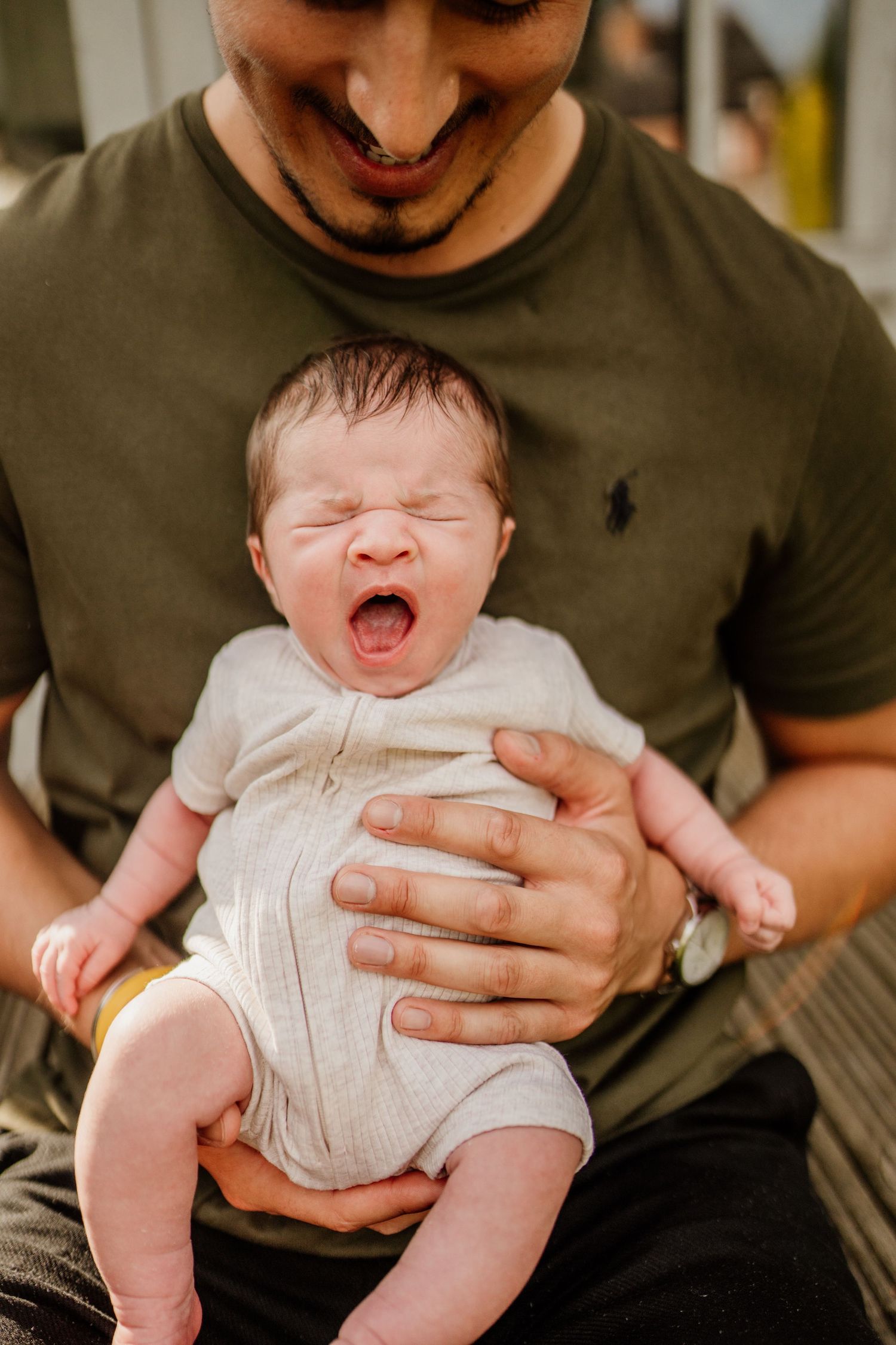 Close-up shots of baby yawning while being held in white onesie.