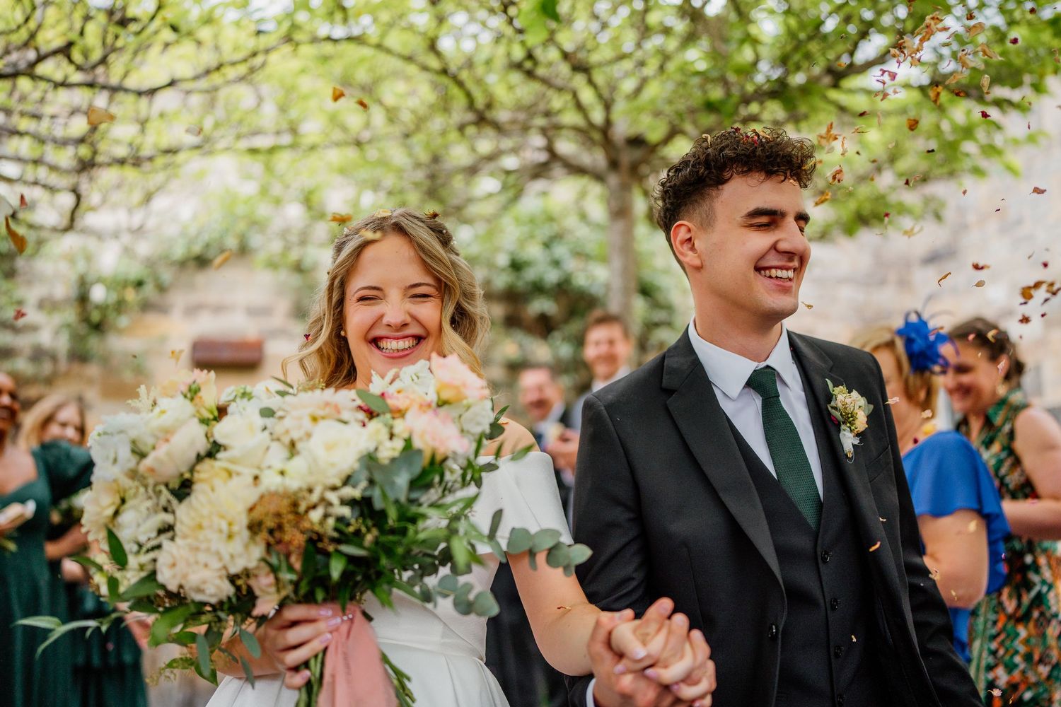 A joyful wedding couple walking together outdoors with a stunning white floral bouquet.