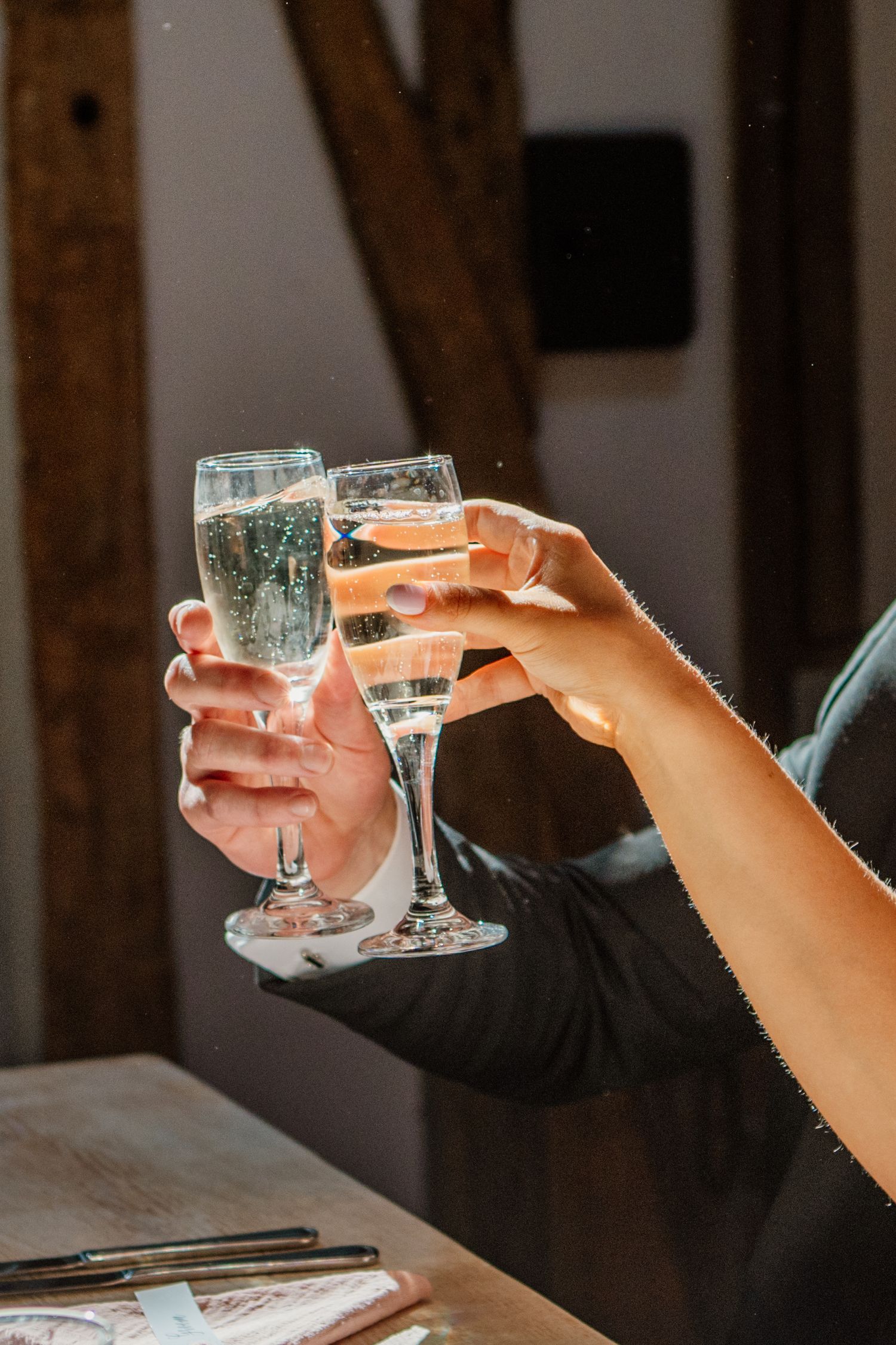 Close-up of hands toasting with wine glasses in rustic venue setting.