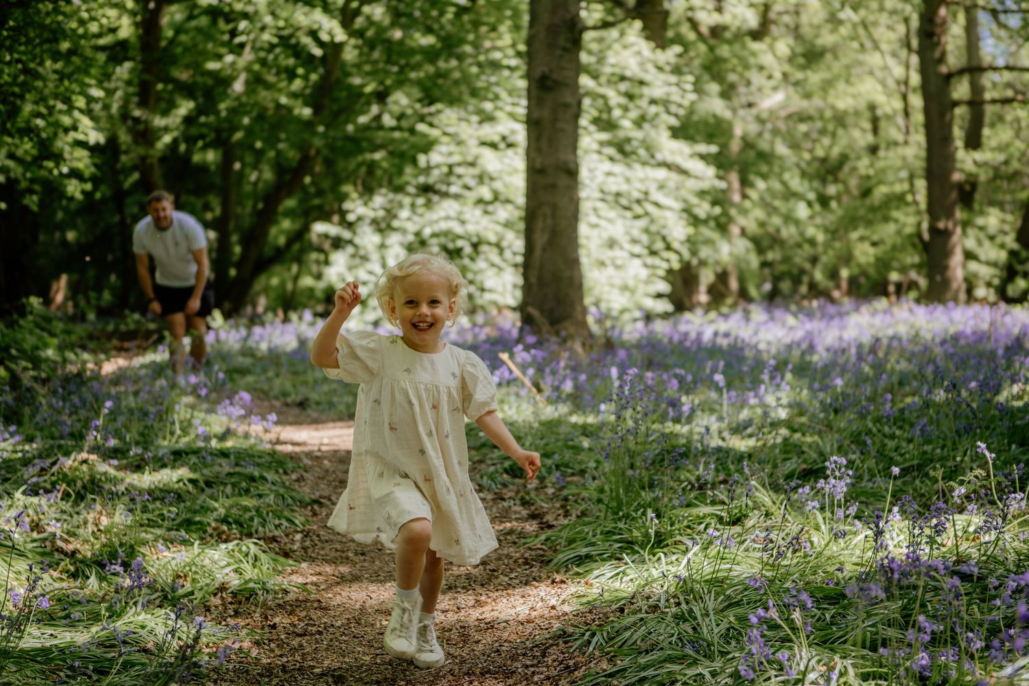 little girl in white dress runs through fields of bluebells in Hertfordshire