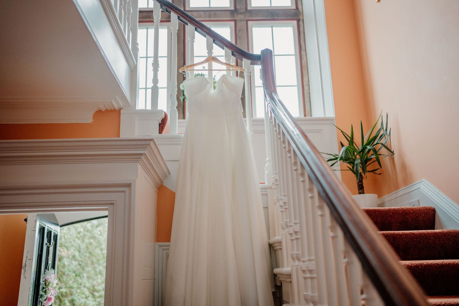 A sunlit staircase with white railings and peach-colored walls in an elegant interior.