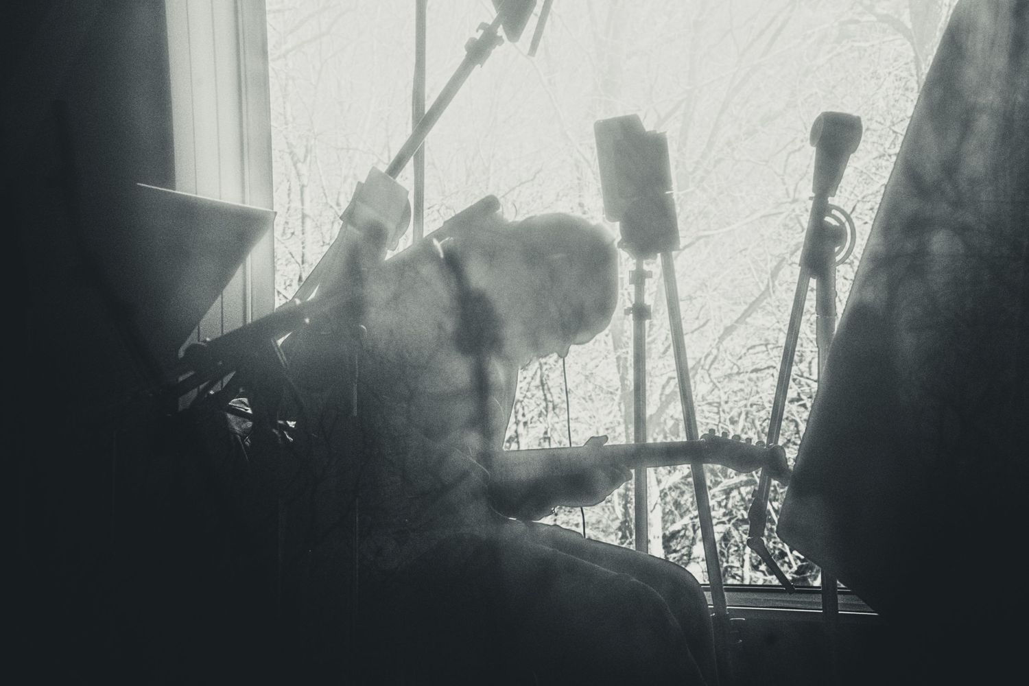 Black and white photo of a fluffy cat resting near a window with microphone stands in a music studio.