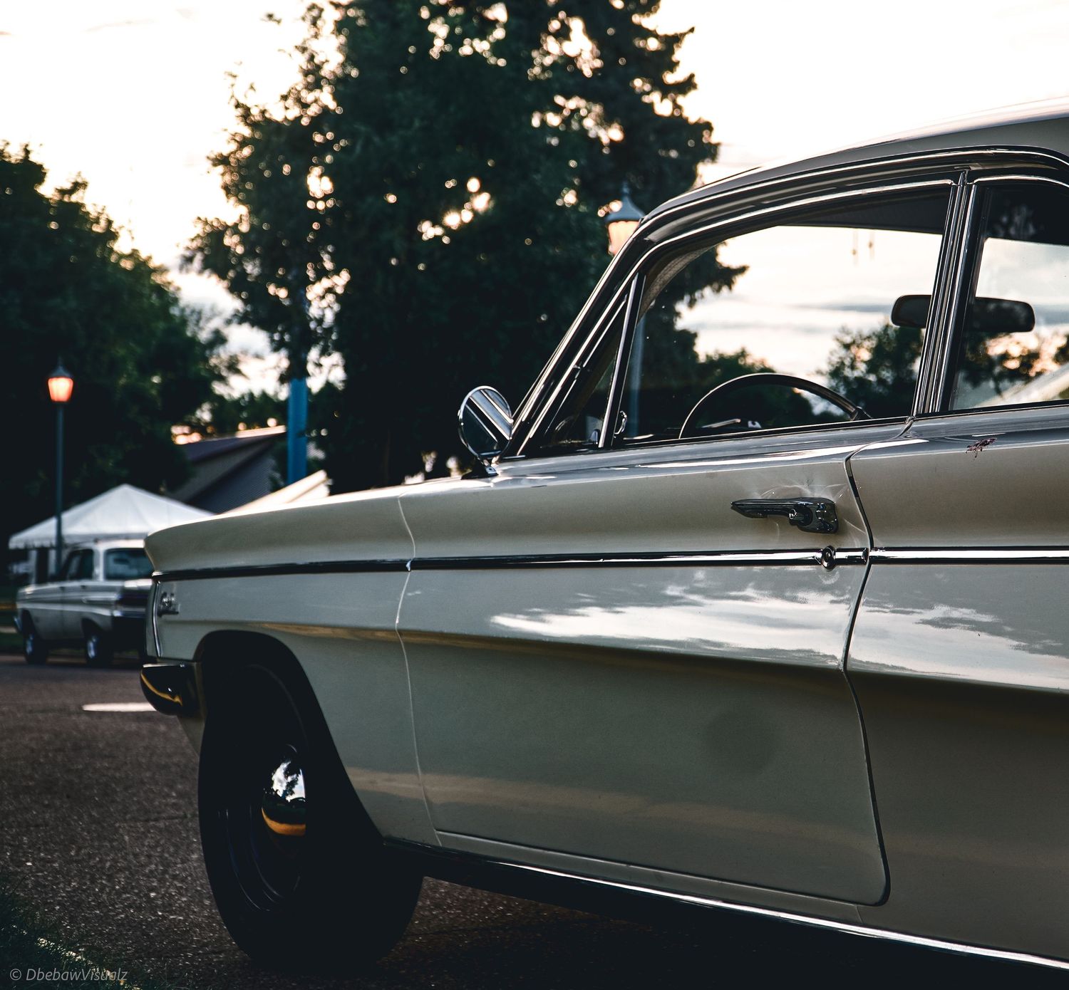 A classic vintage white car parked outdoors at dusk with trees in the background.