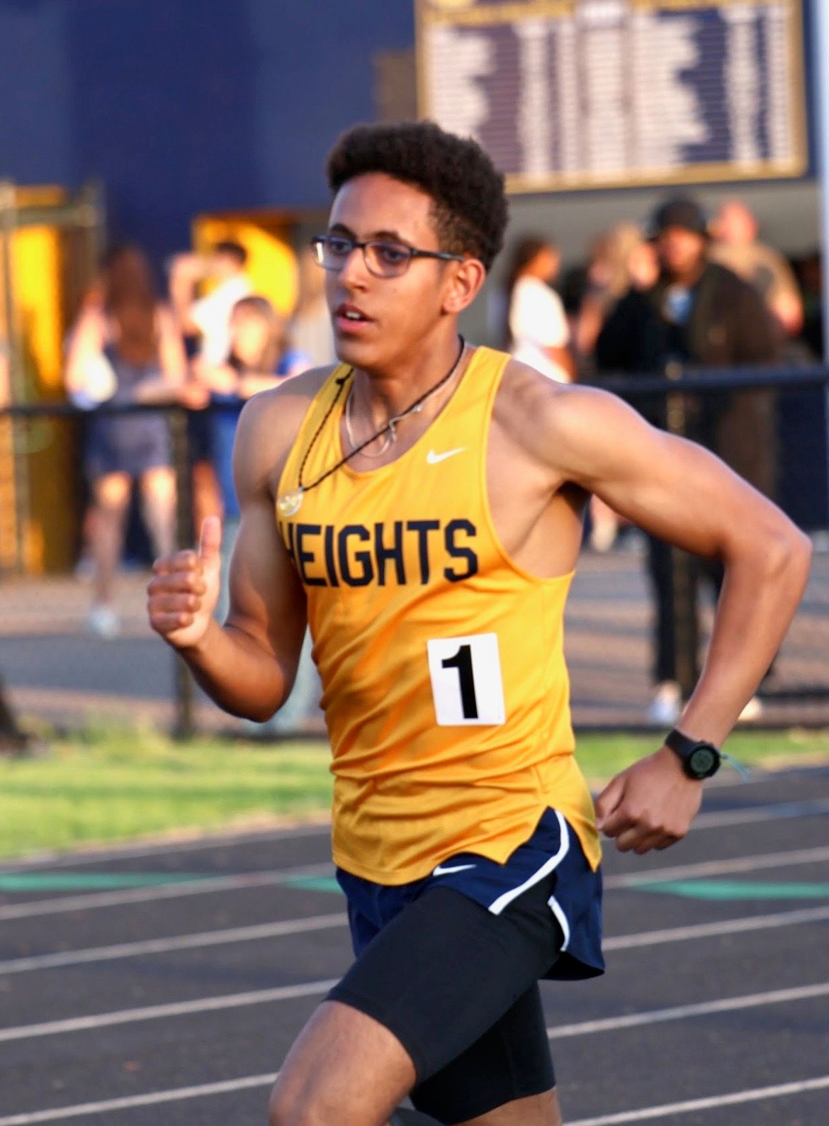 A track athlete in a yellow jersey competes in an 800m race on an outdoor track.