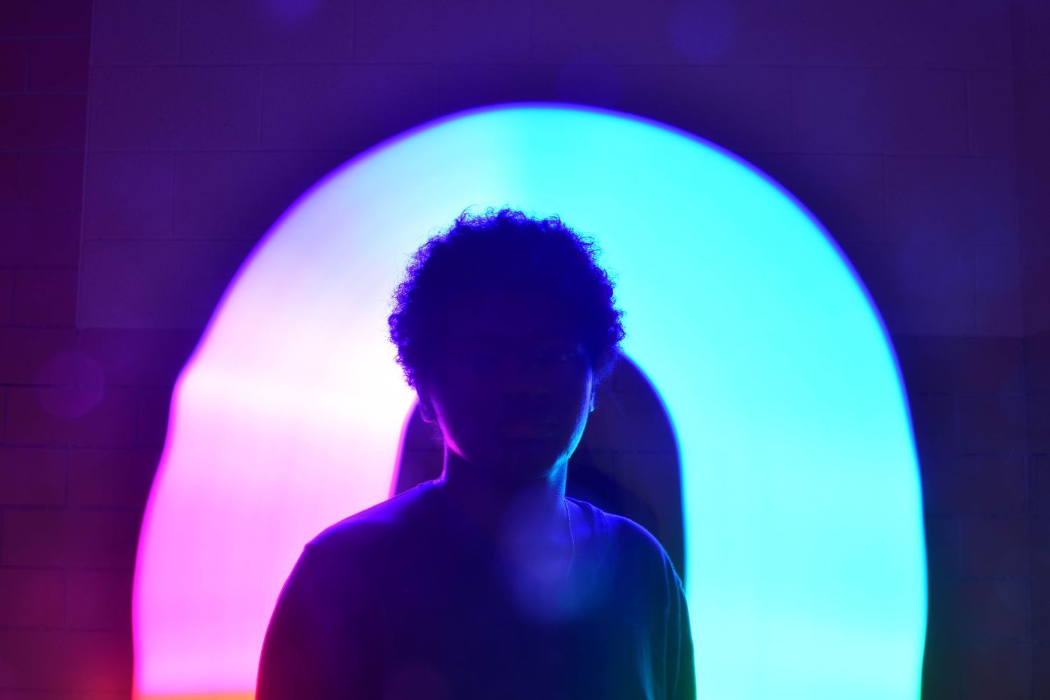 Silhouette against a glowing neon circle with pink and blue gradient lighting.
