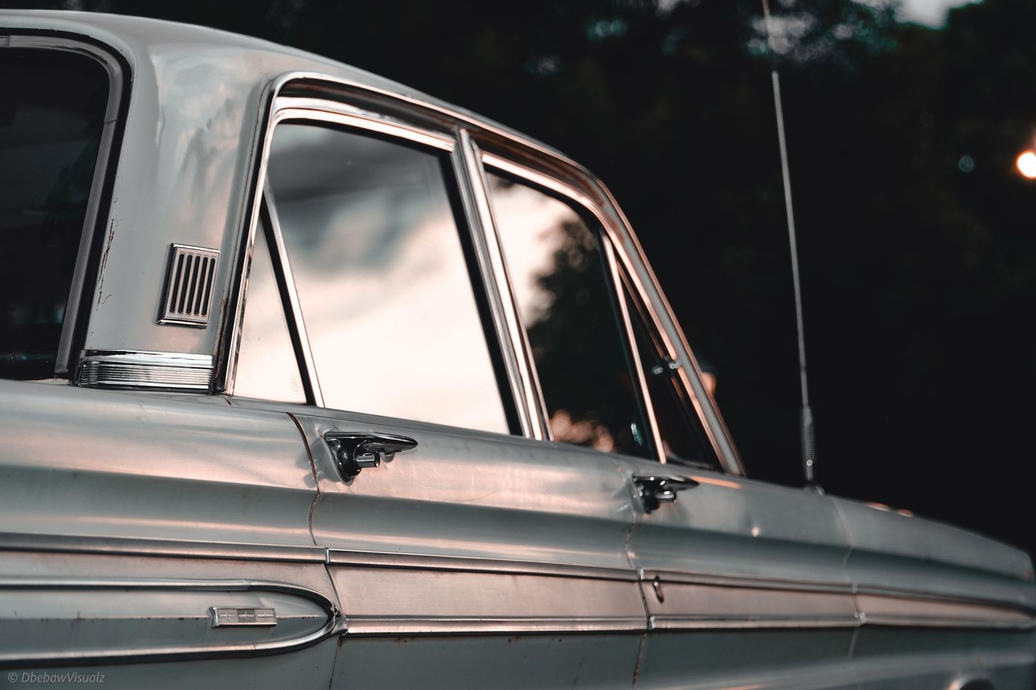Vintage classic car side profile with chrome details and reflective windows in moody outdoor lighting.