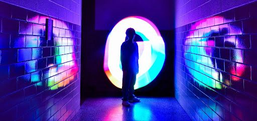 Silhouette standing in neon-lit corridor with circular portal glowing in pink and blue.