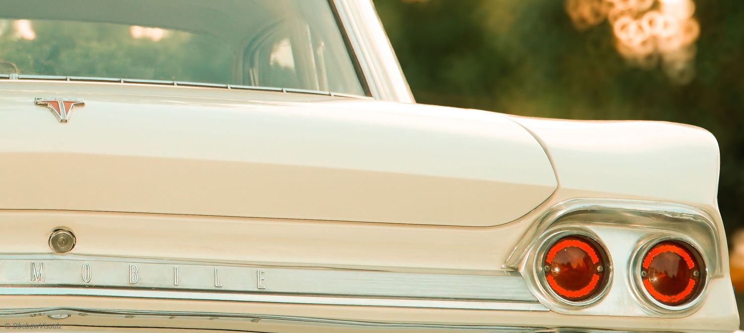 Vintage white classic car rear view showcasing iconic tail fins and red taillights in warm sunlight.