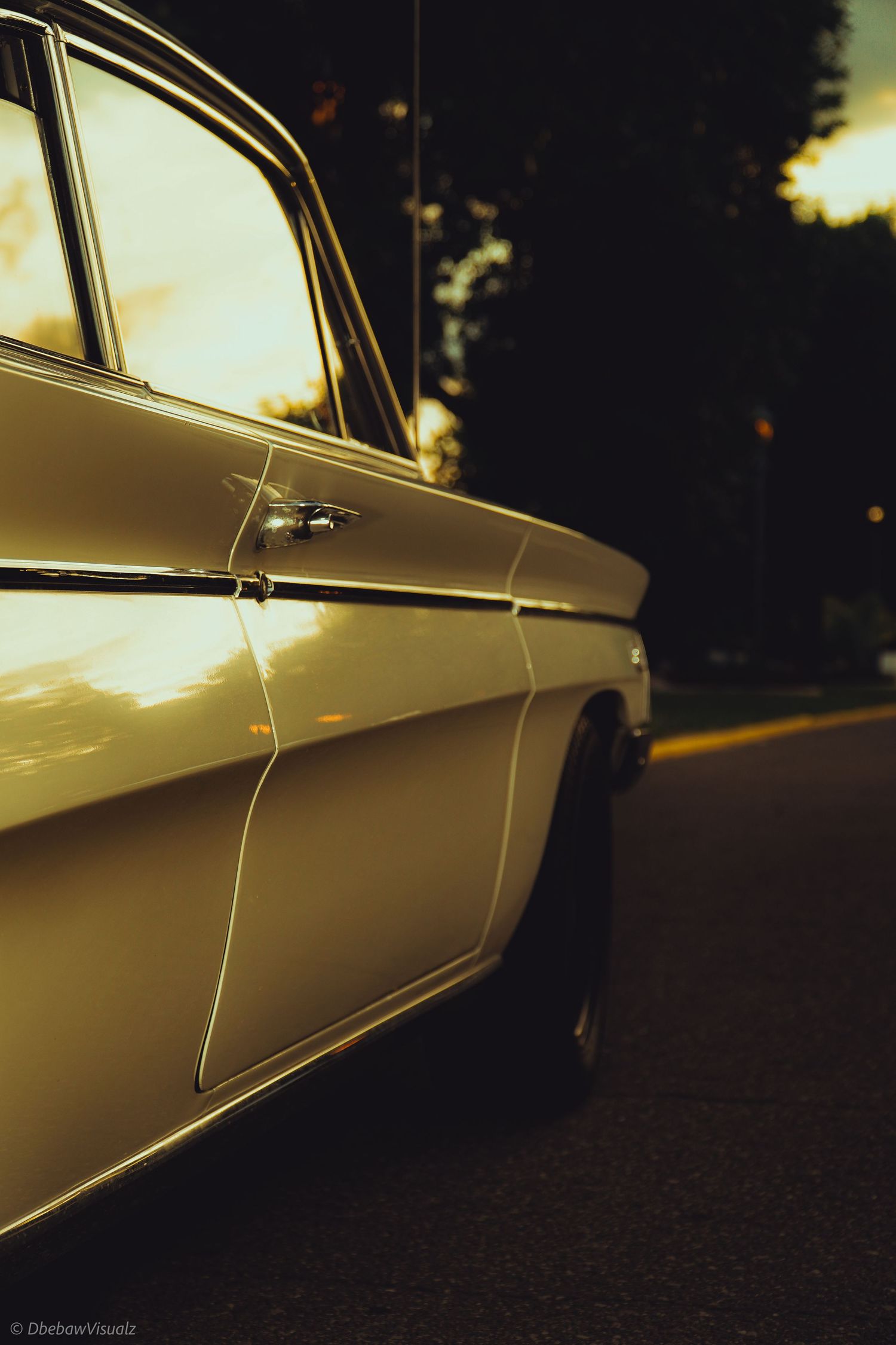Vintage classic car shot at golden hour sunset, showcasing chrome door handle and sleek body lines on empty road.